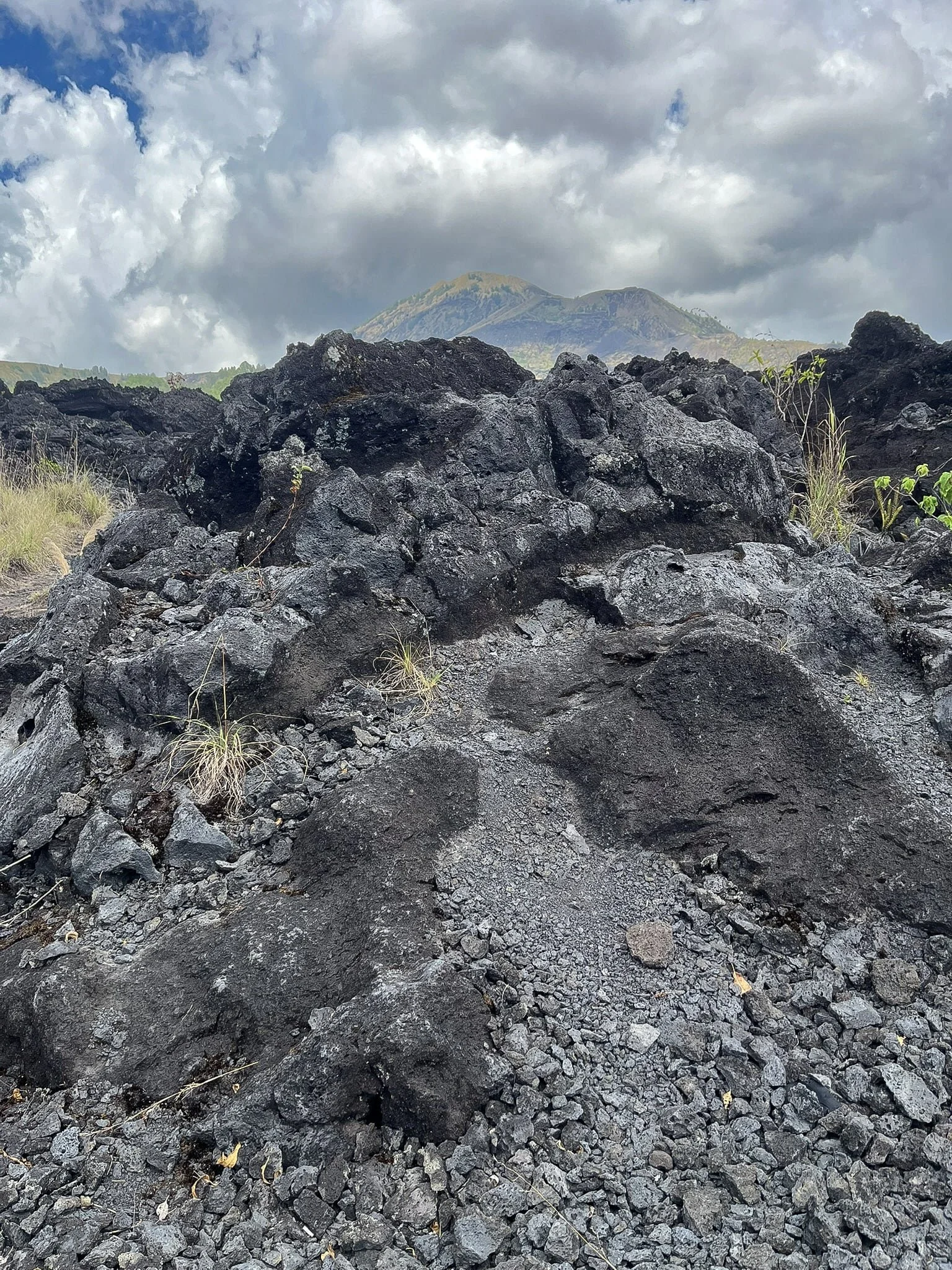 Close up of black volcanic lava rocks from Mount Batur eruption with volcano in background, Kintamani Bali