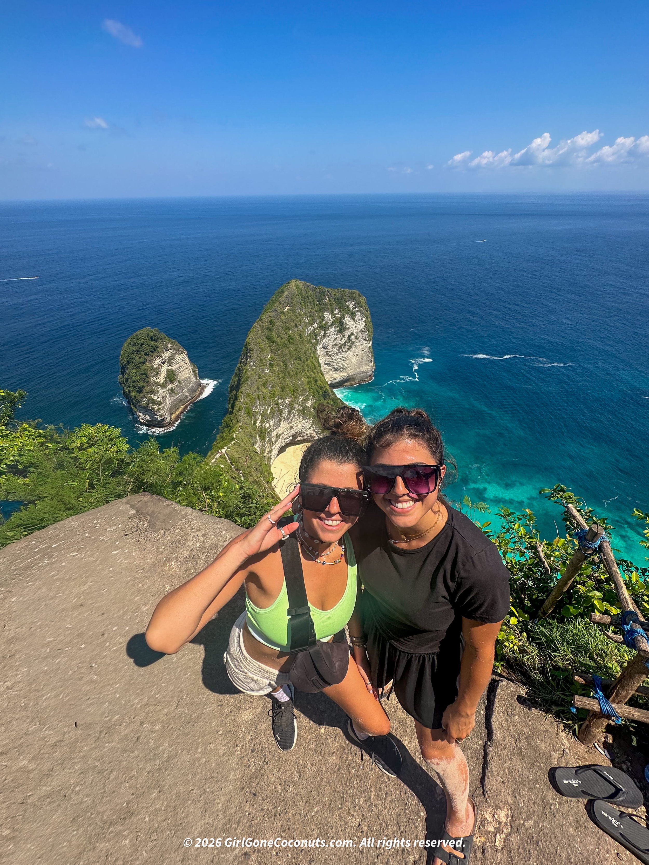 Travelers standing atop the famous Kelingking Beach viewpoint with turquoise waters and green limestone cliffs.