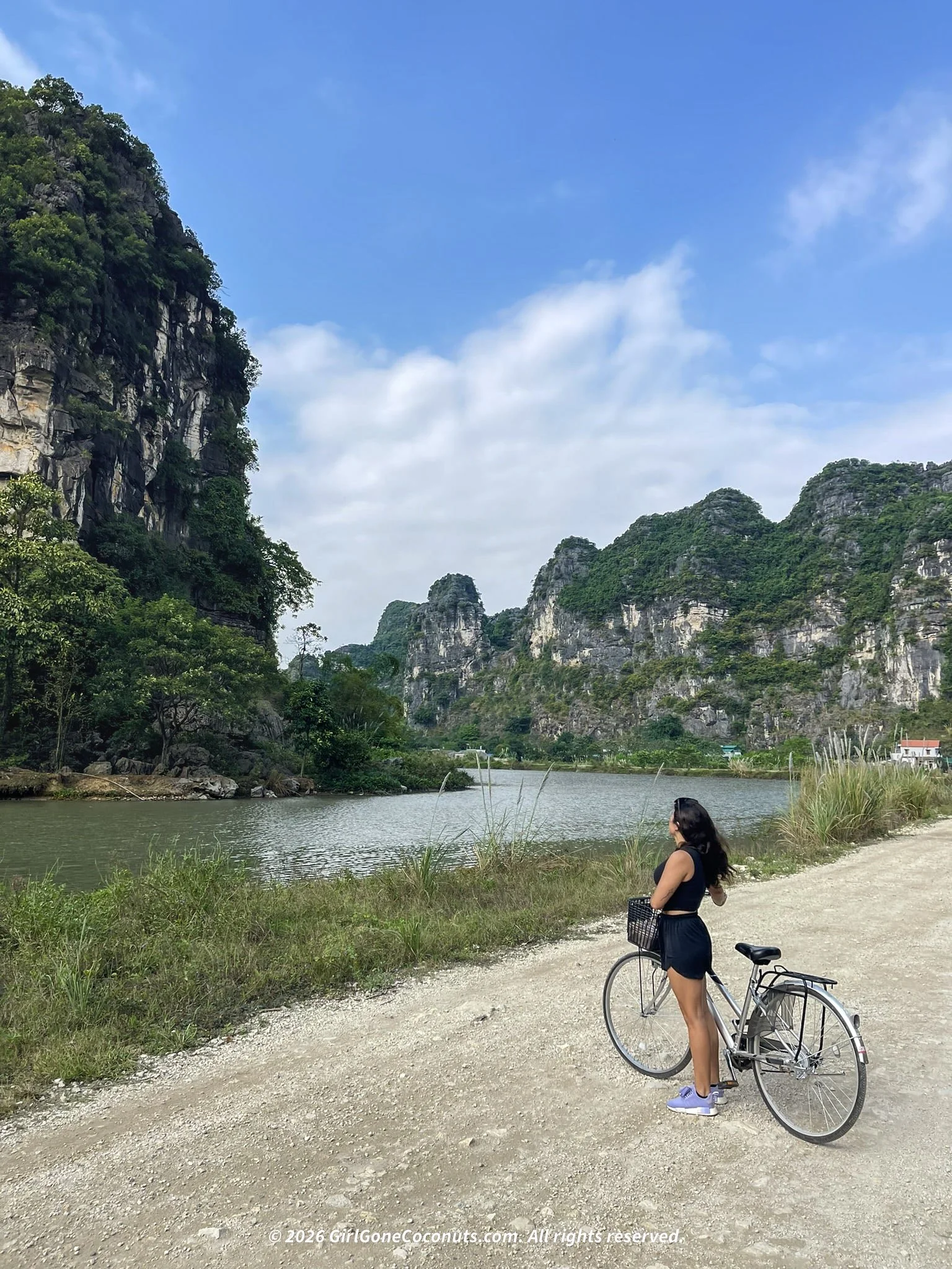 Cyclist standing with a bike along the river surrounded by limestone karsts in Ninh Binh, Vietnam