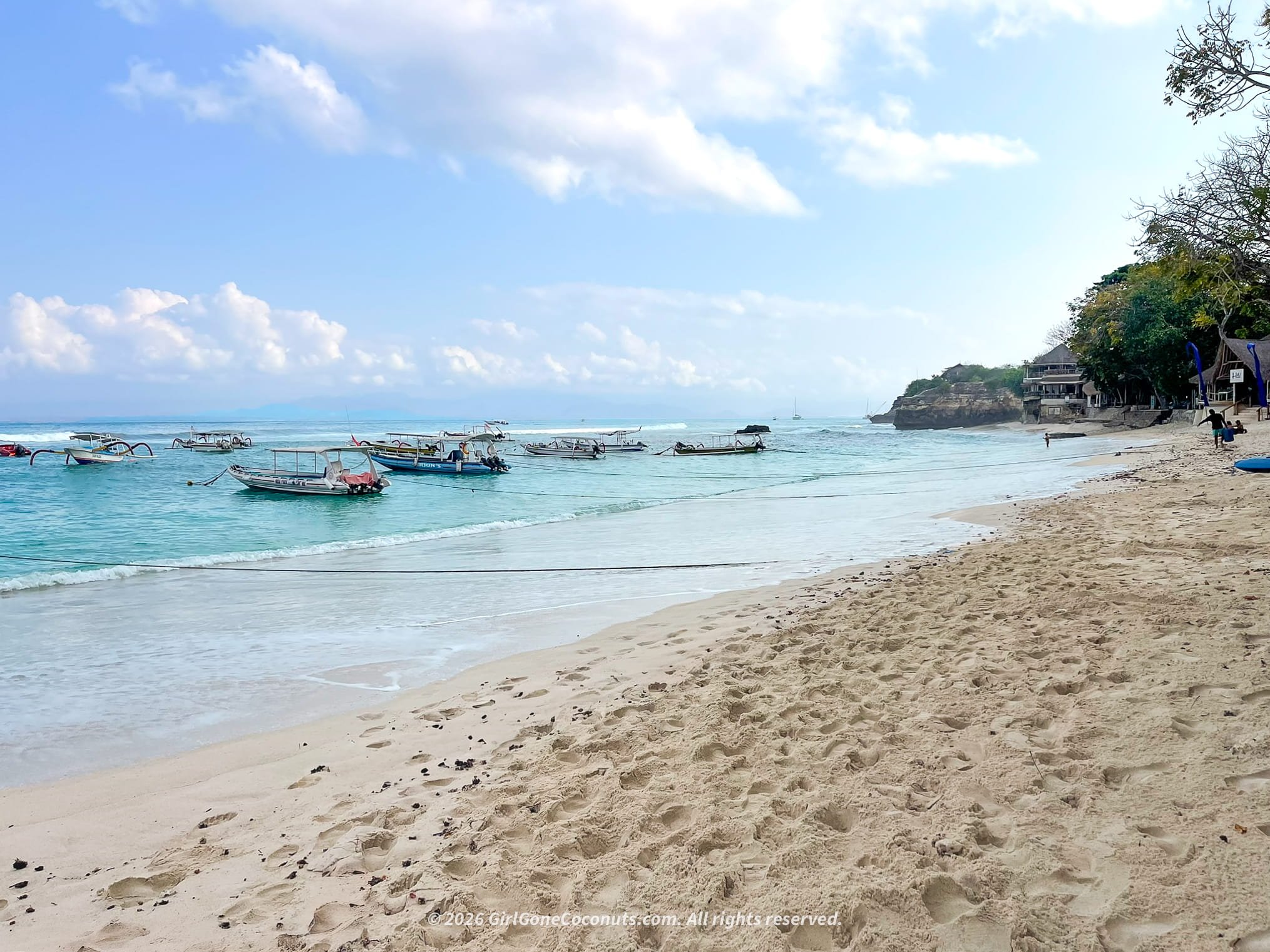 Mushroom Bay Beach in Nusa Lembongan with clear turquoise water, sandy shoreline, and traditional boats floating in the bay.