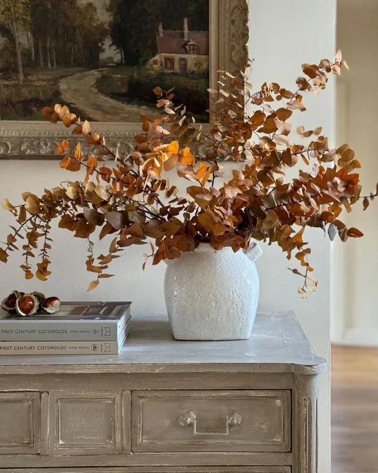 Autumn home décor with a rustic dresser, white vase of dried eucalyptus, warm fall tones, and a cozy cottage-inspired vignette.