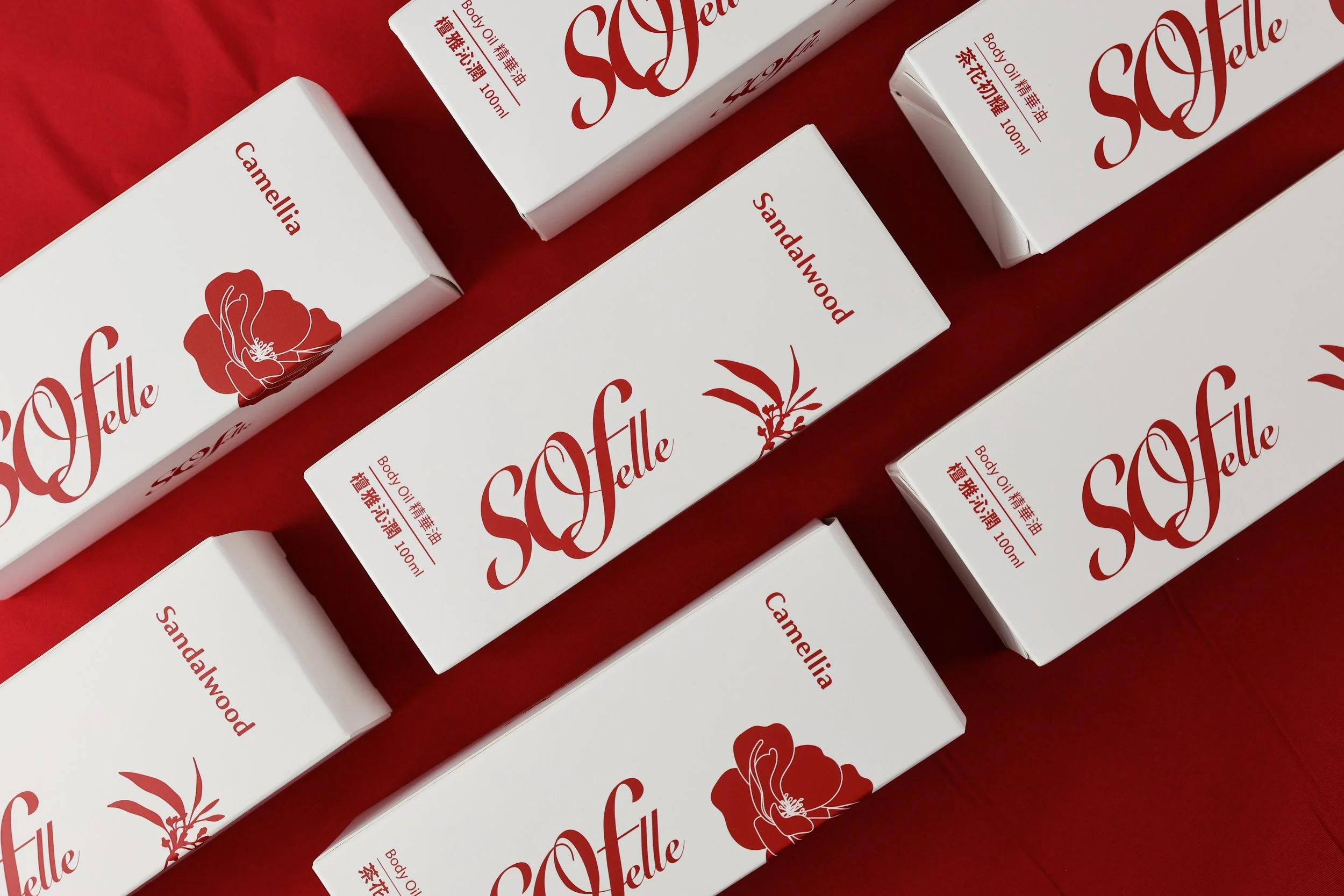Multiple white boxes of Scarlett body oil with red floral and plant illustrations, arranged on a red surface.