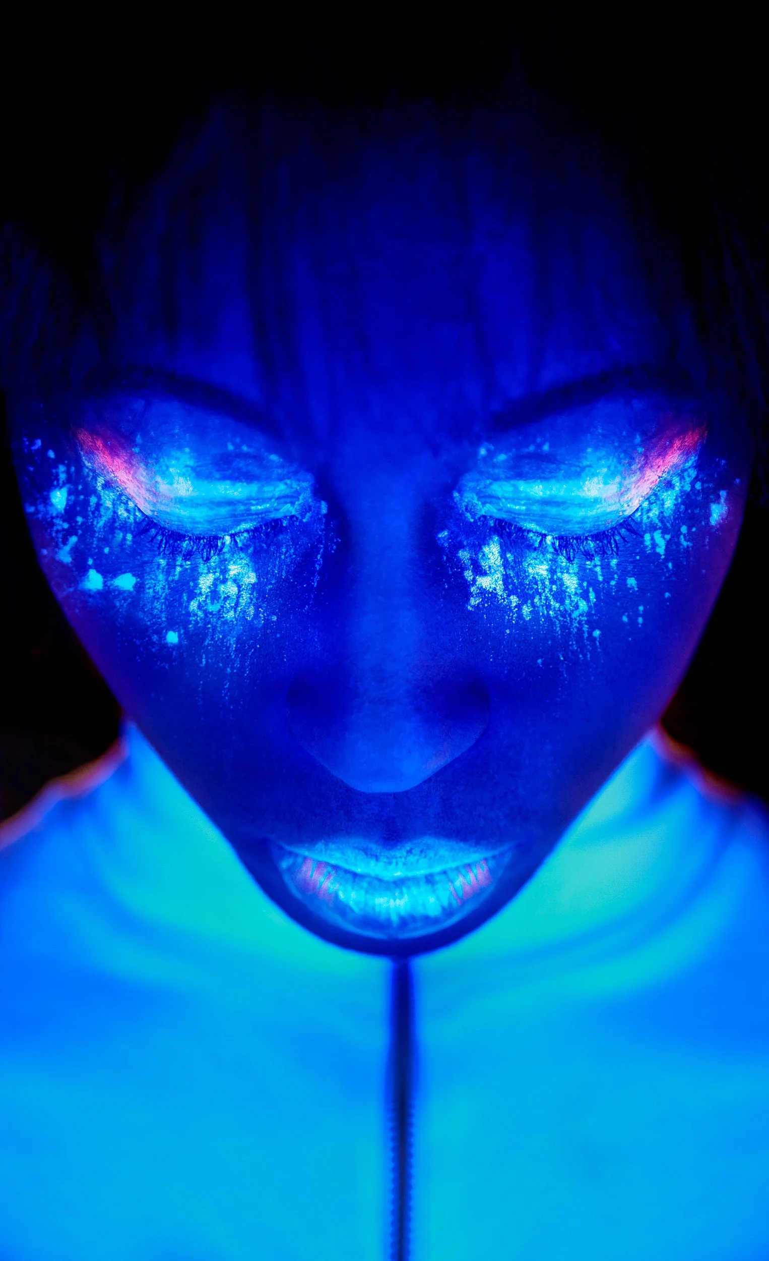 Close-up of female model with face illuminated by blue UV light, eyes closed, wearing glowing makeup. Photography by Dave Wall Photo