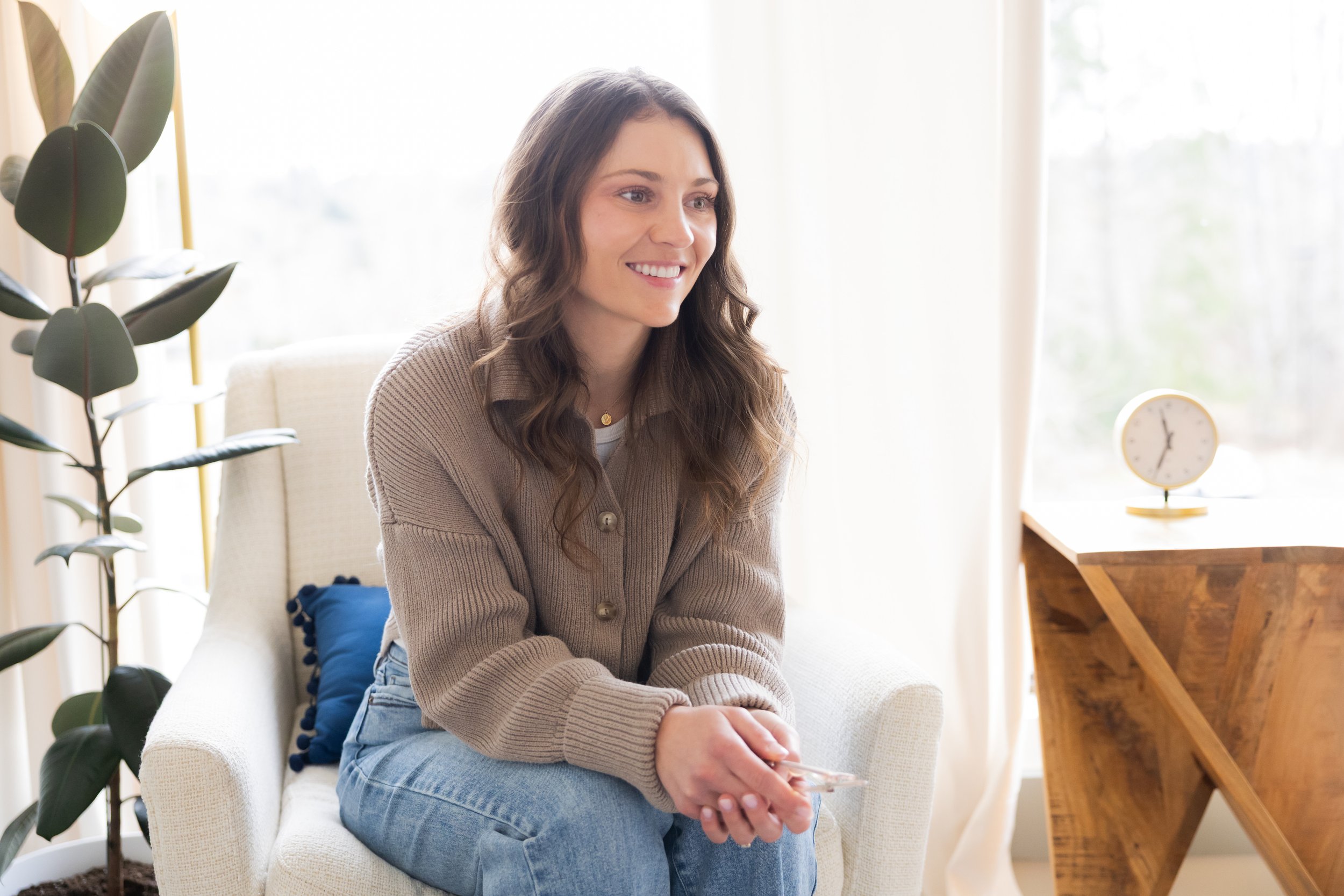 Bellevue therapist for athletes recovering from injury and rebuilding mindset, sitting on a white armchair, smiling.