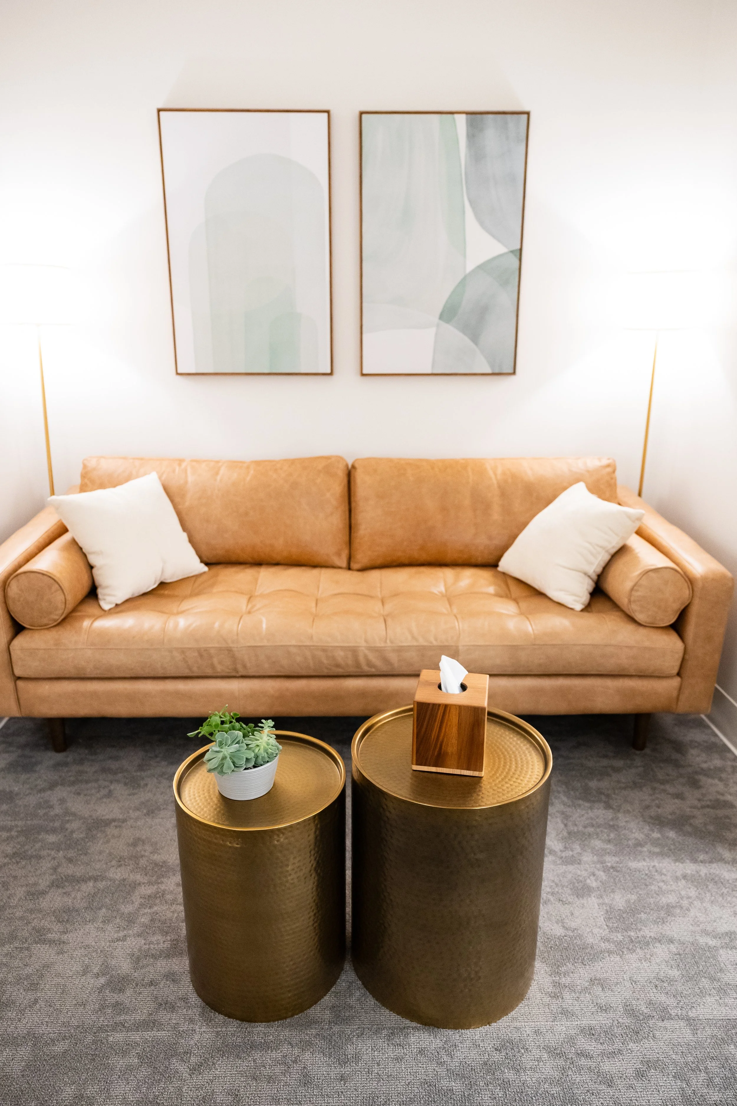 Modern Bellevue counseling space designed for comfort, safety, and confidentiality, with a tan leather sofa, white pillows, two gold cylindrical side tables.