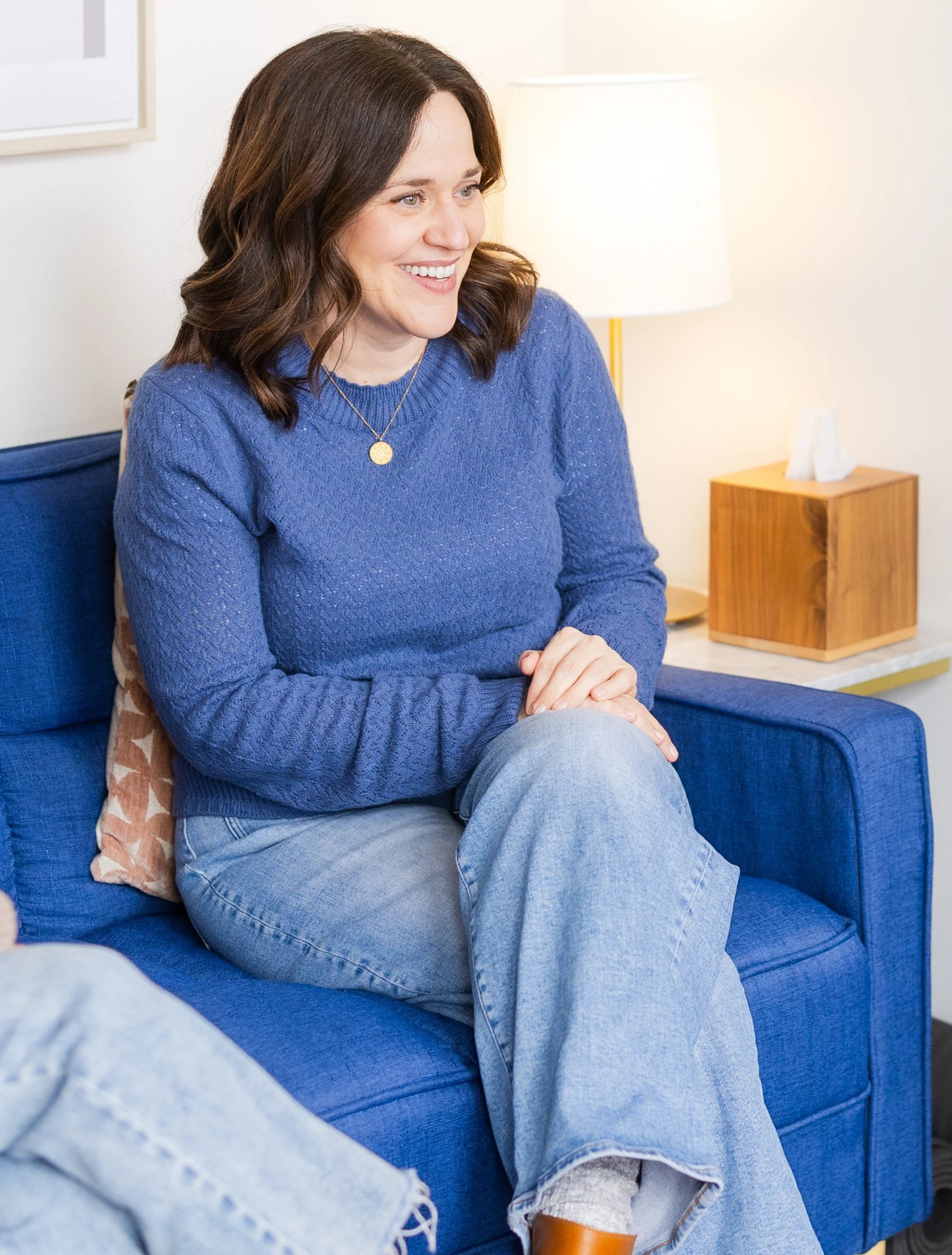Couples counseling in Bellevue, WA for communication issues and rebuilding trust. Therapist sitting on a blue couch in the in-person couples counseling office. She is smiling and looking to the side.
