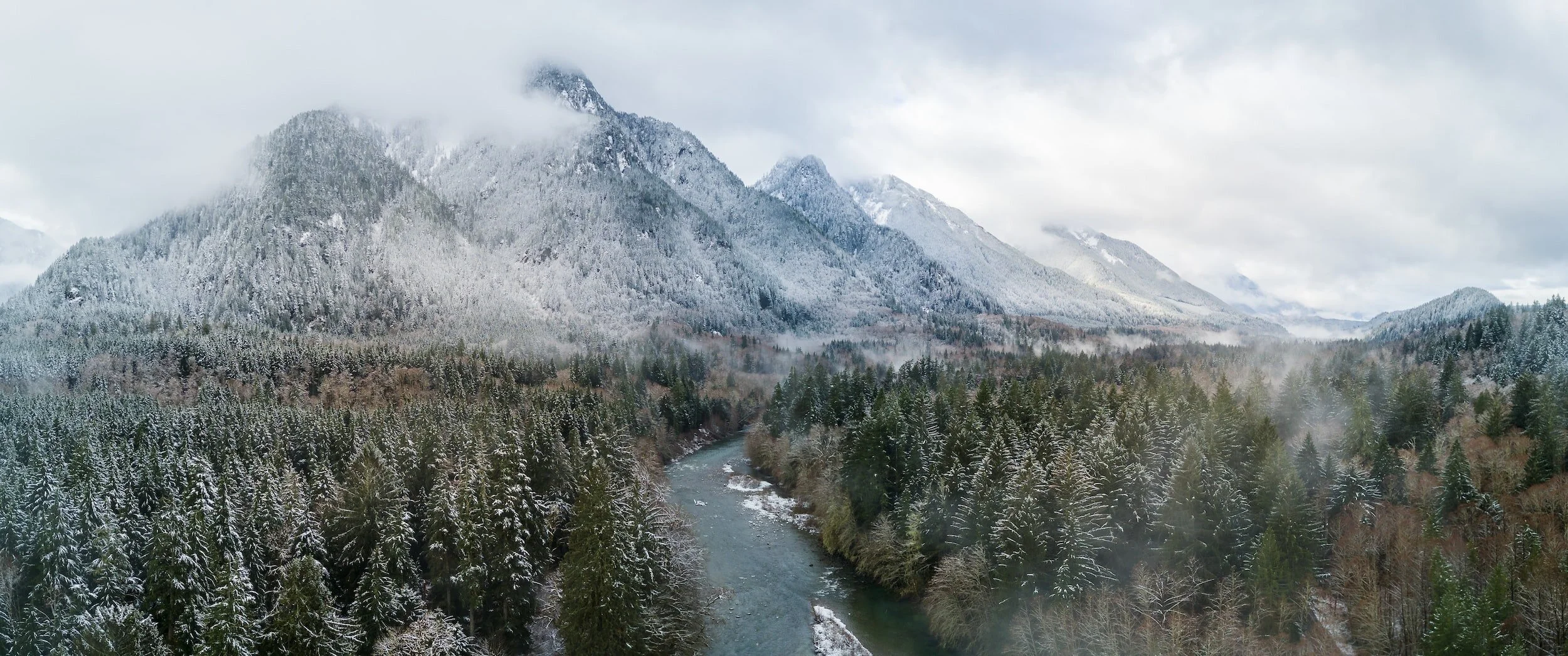 mountains covered in snow above trees and river