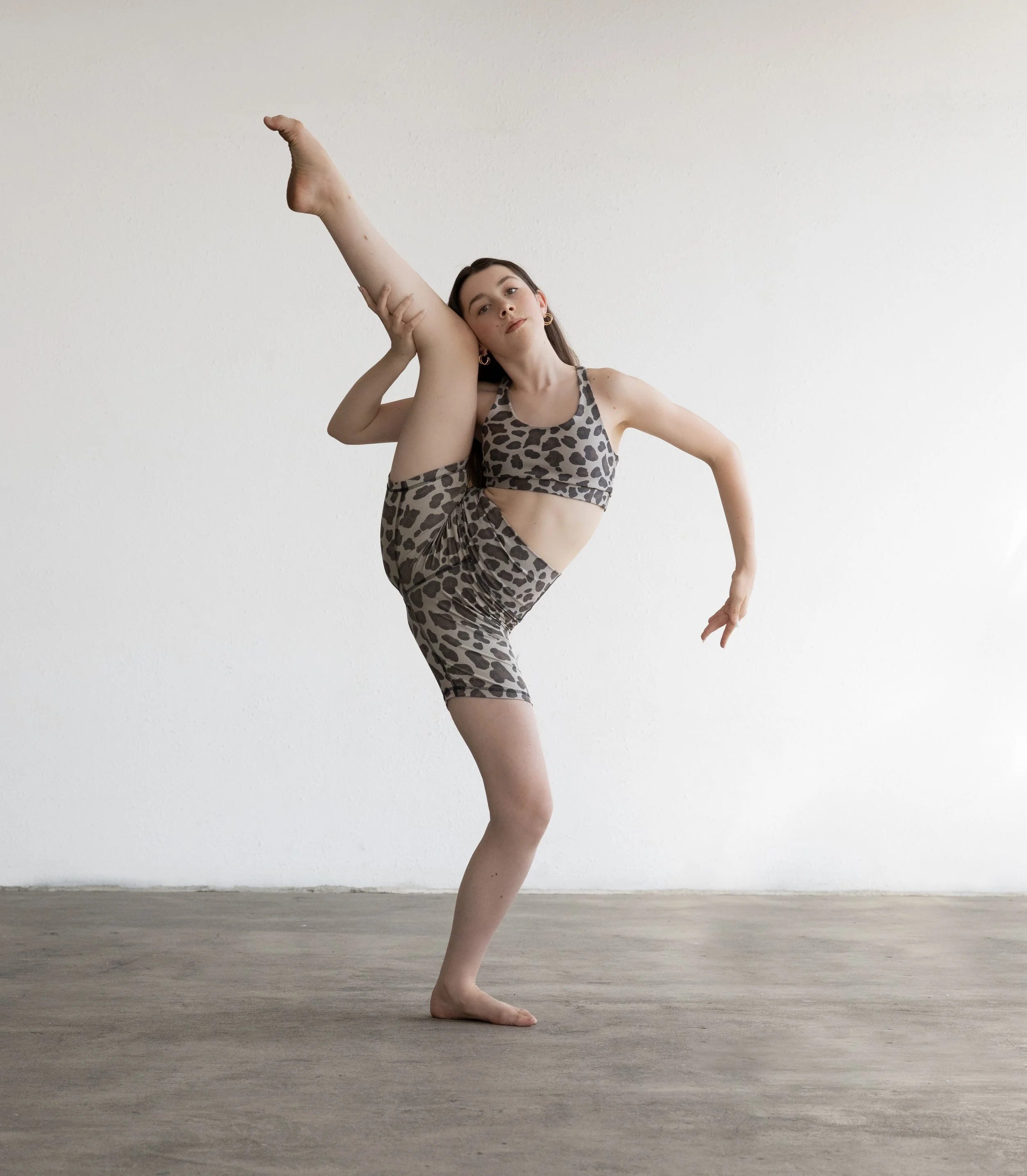 Woman in leopard print activewear performing a high leg stretch in a studio.