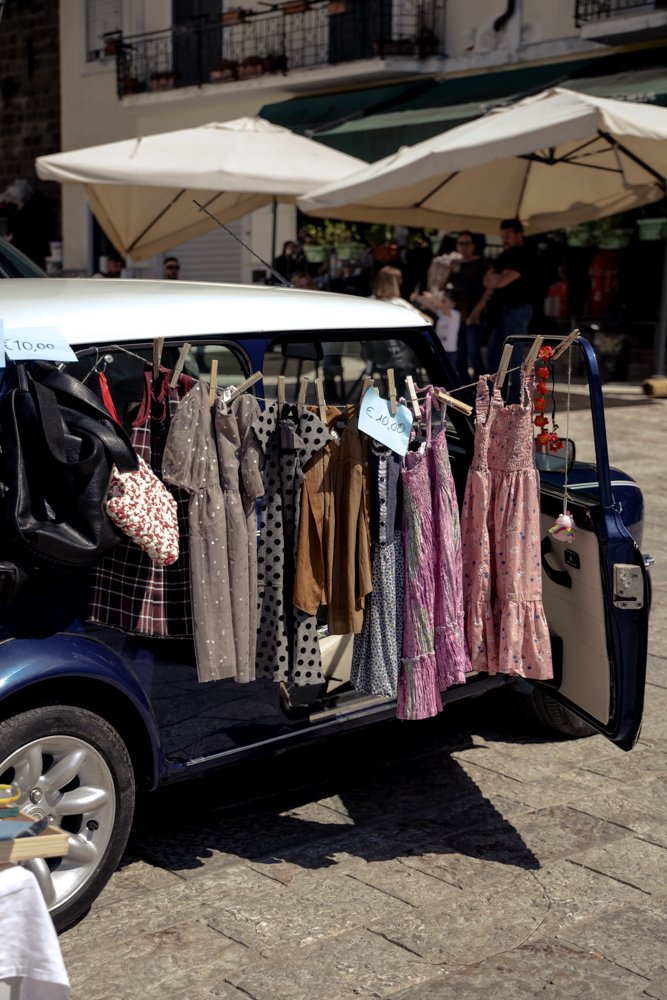 Vestiti colorati appesi a una macchina in un mercato all'aperto con ombrelloni bianchi sullo sfondo.