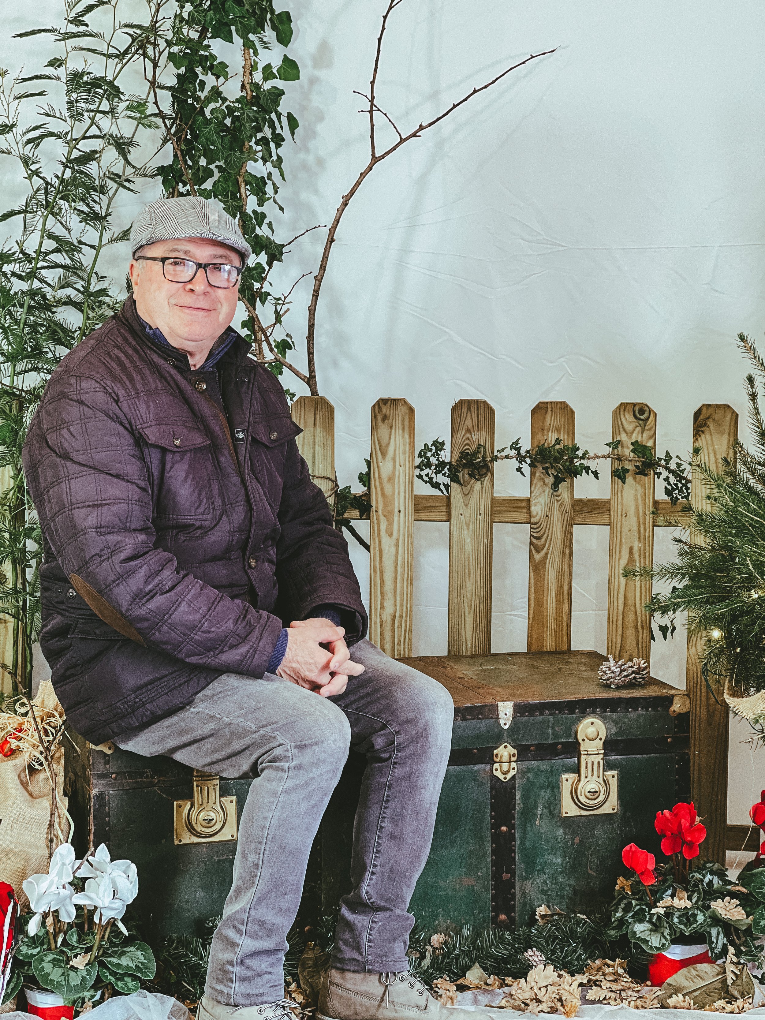 Uomo seduto su un baule decorato con piante e fiori in un ambiente rustico.