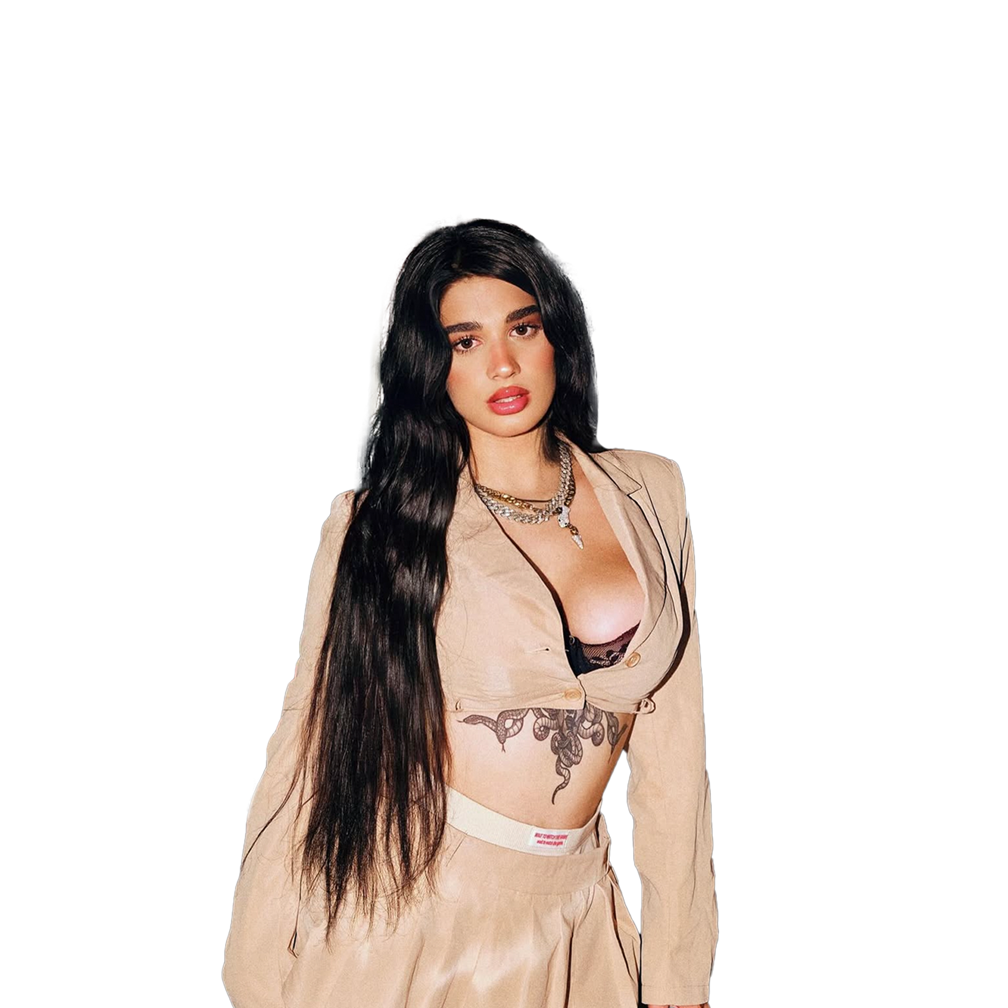 A woman with long dark hair, wearing a beige blazer, black lace bra, and beige pants, accessorized with necklaces, posing with a confident expression. isyourgirlangie