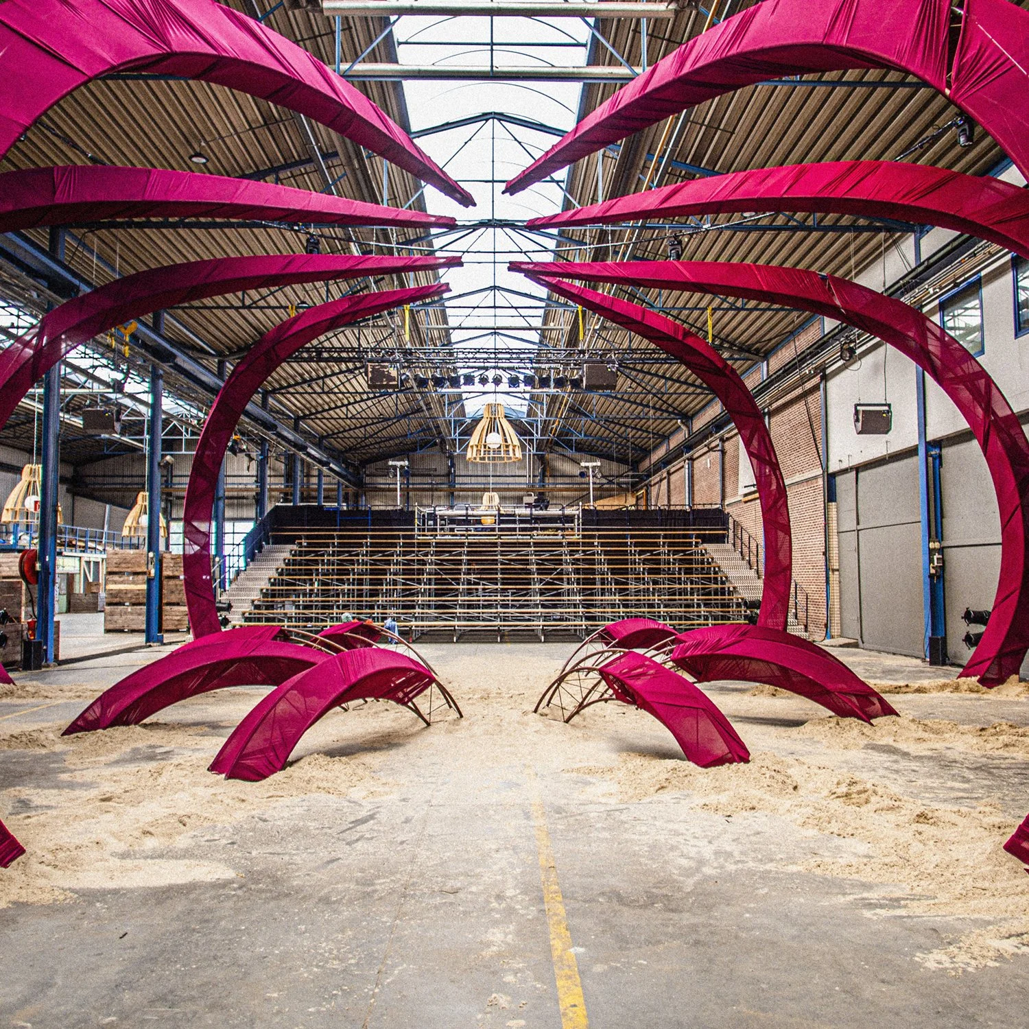 Binnenruimte met zand, structuur van rood metalen decoratie in de vorm van bladeren of vruchten, en tribune met houten banken.
