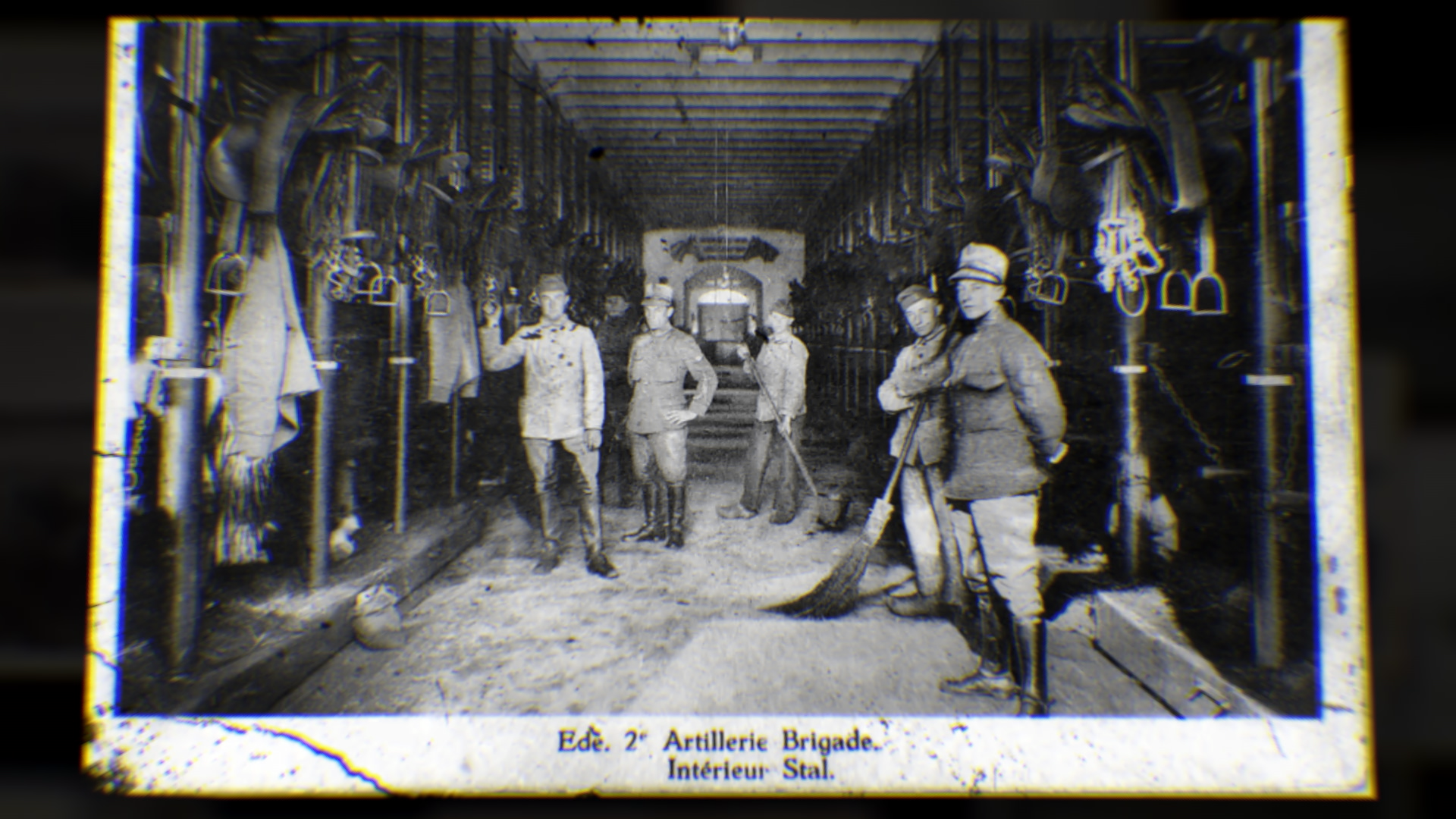 Zes mannen in oude militaire uniformen staan binnen in een houten schuur, omringd door wapens en uitrusting, met een portaallamp in de achtergrond. Volgens de tekst onderaan is het een artilleriebrigade van het tweede regiment, met interieur van de stallen.