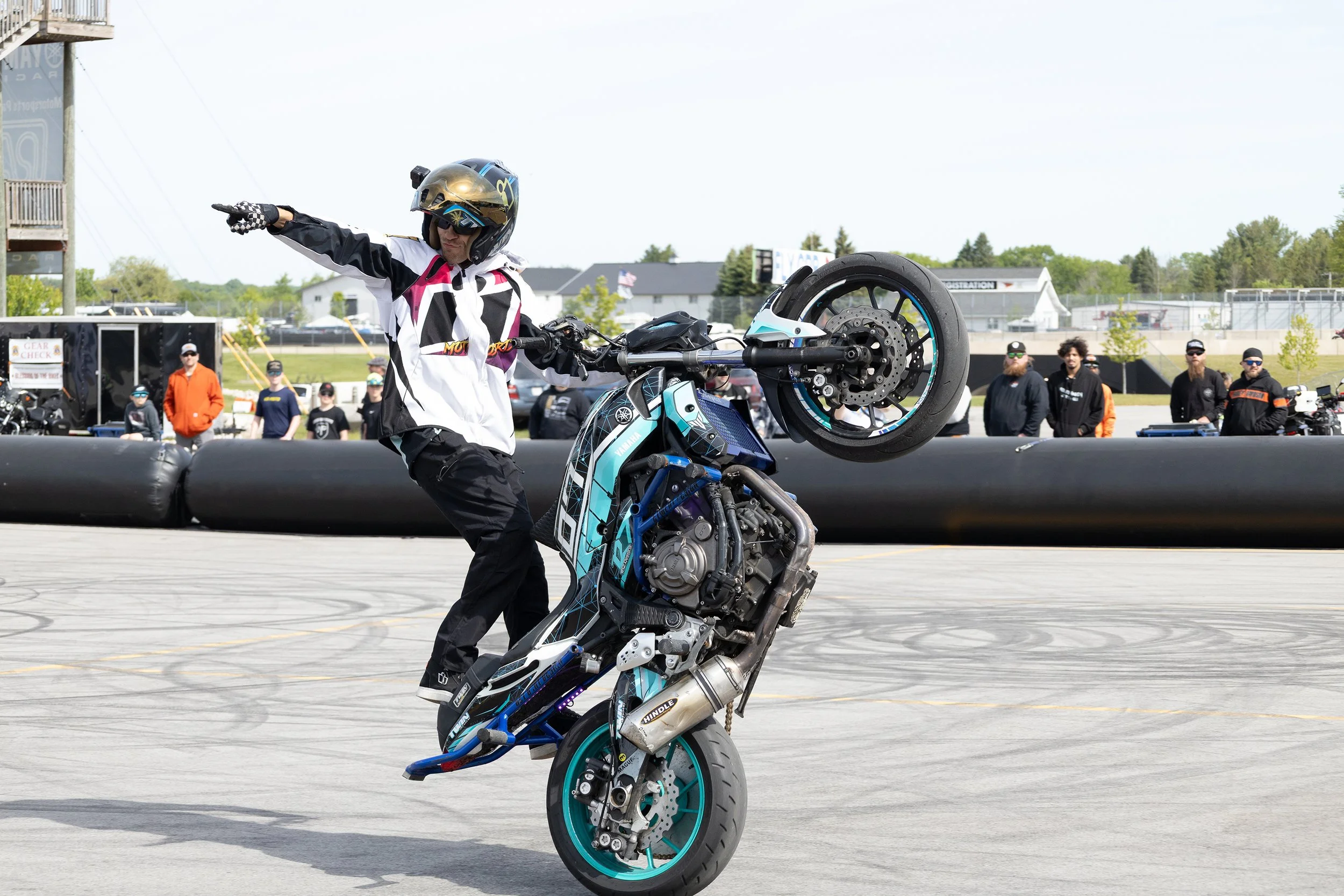 A motorcyclist performing a stunt on a dirt bike at a motorcycle event, with a crowd of spectators in the background.