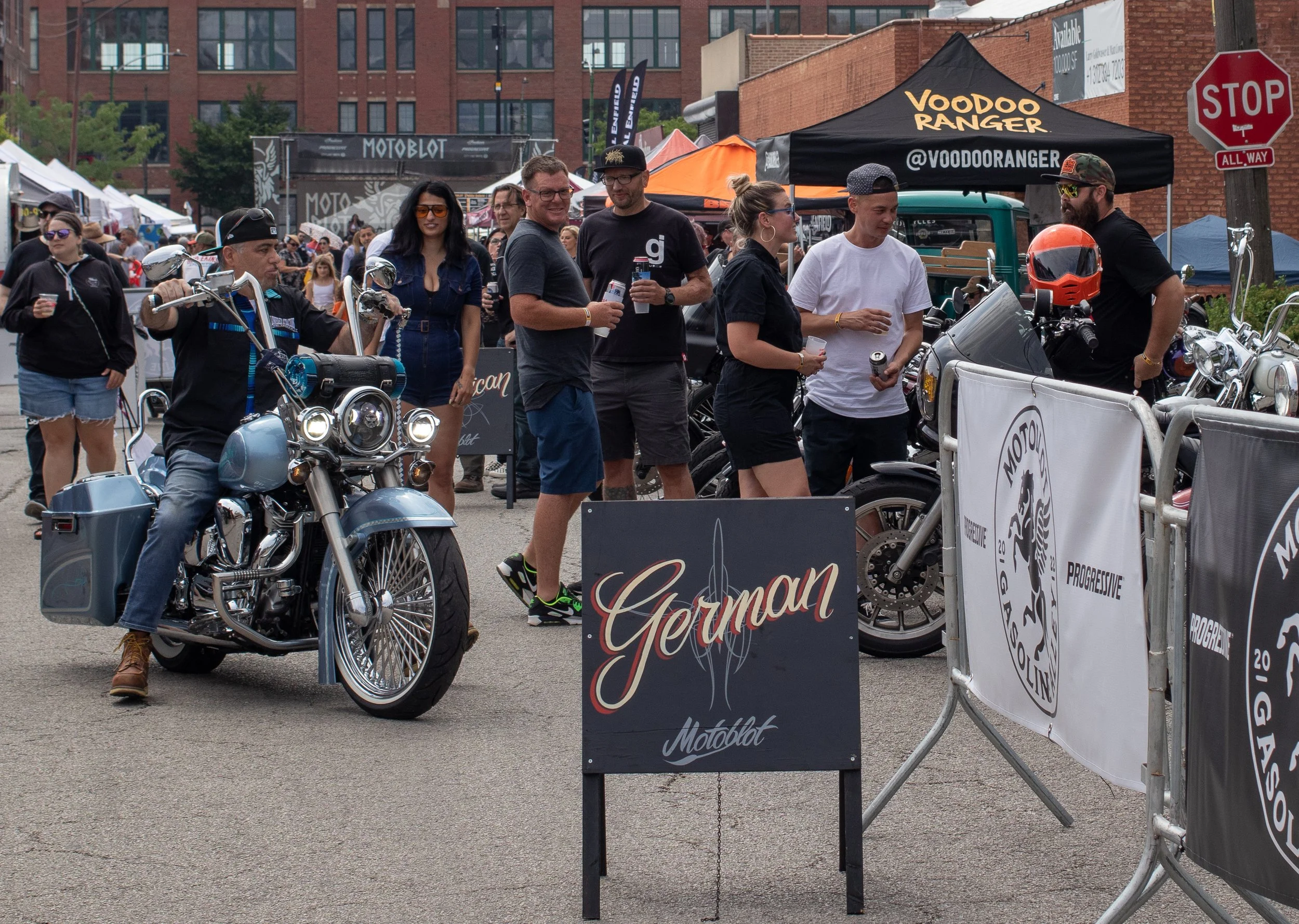 Group of people at an outdoor event with motorcycles, tents, and banners.