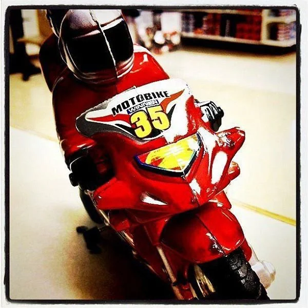 Red toy motorcycle with a racing number 35 and the word 'Motobike Winner' on the front, placed indoors on a light-colored surface.