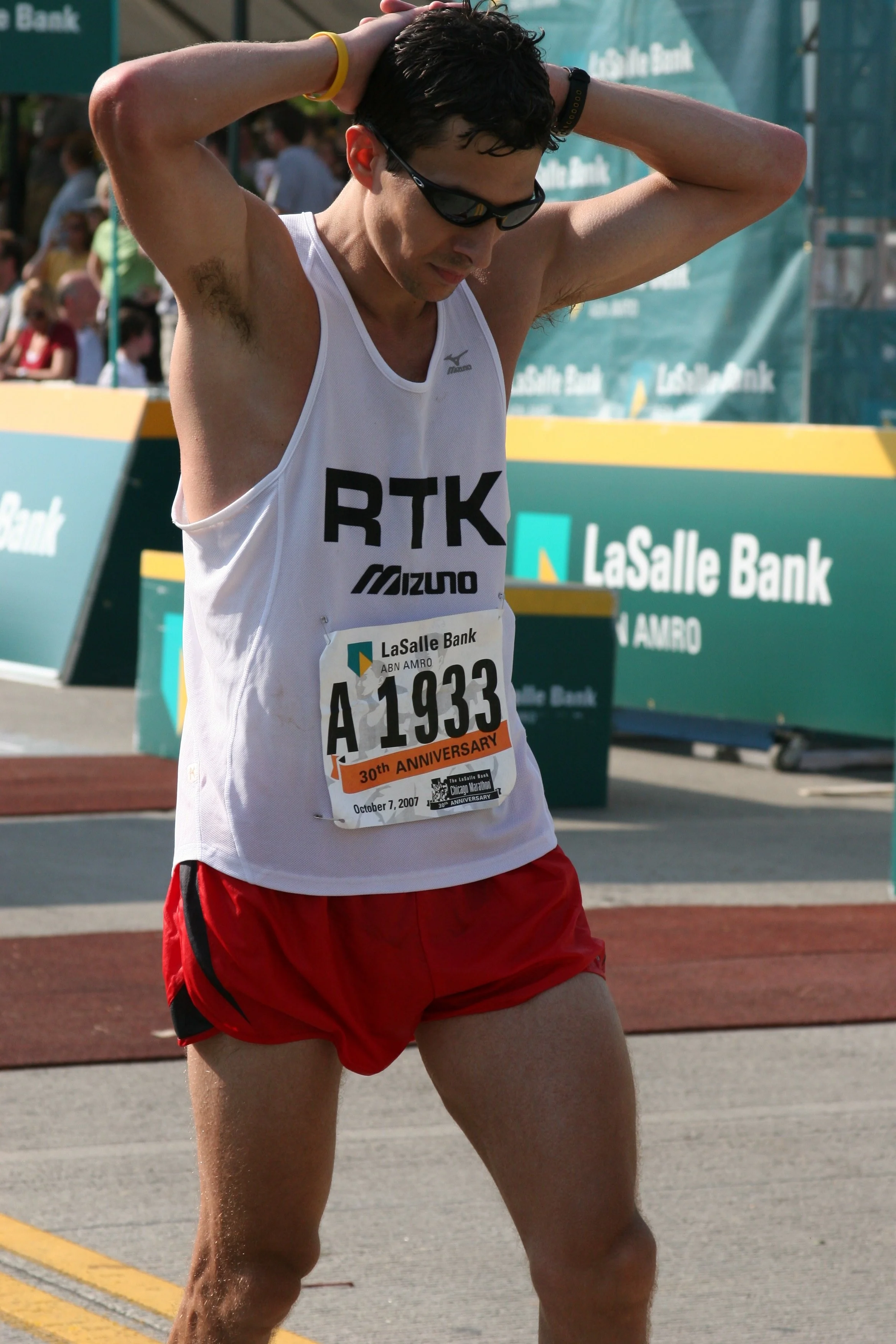A male marathon runner wearing sunglasses, a white tank top, red shorts, and a race bib with the number A 1933, standing with his hands on his head during a race at LaSalle Bank Chicago Marathon on October 7, 2007.