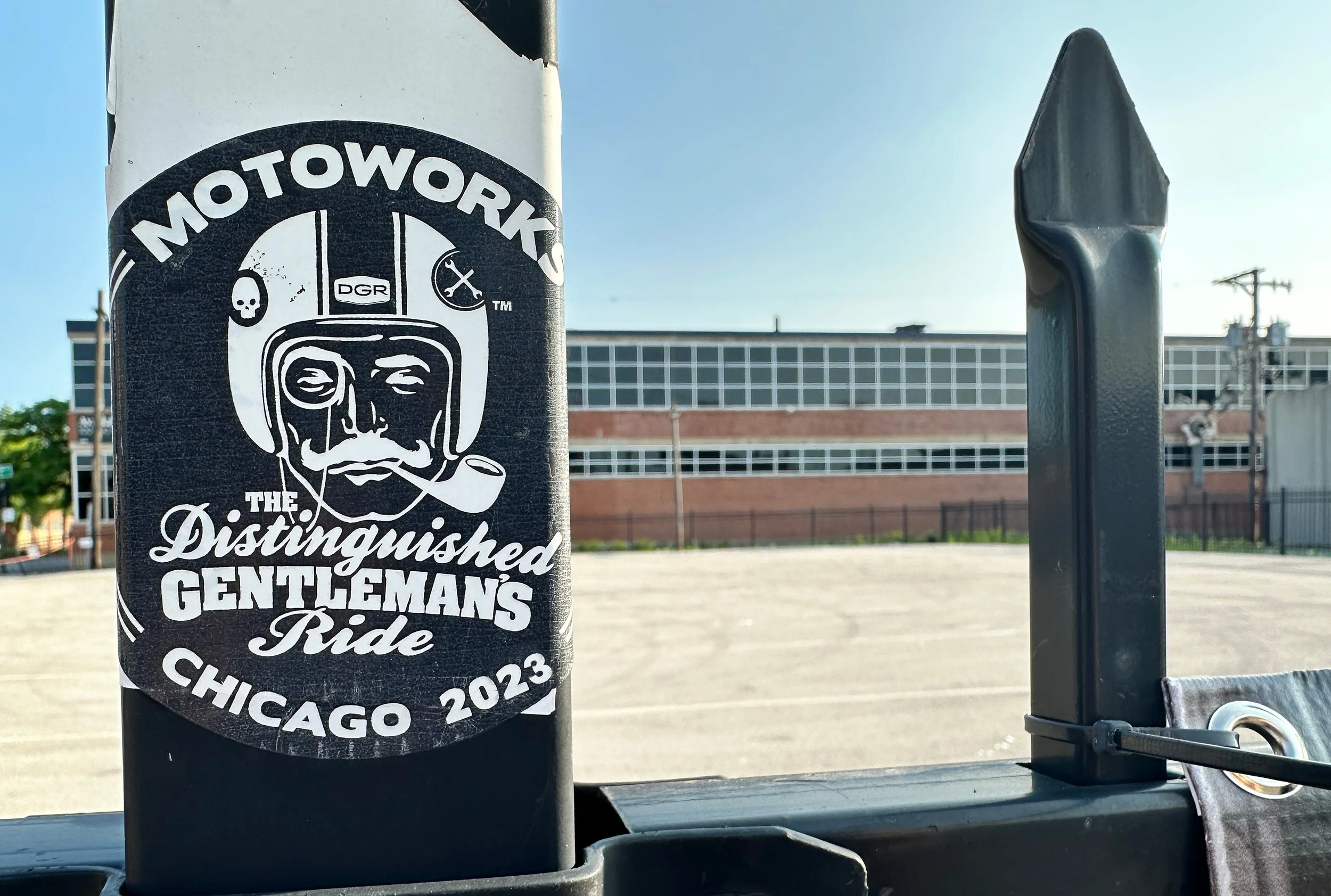 A black circular sticker on a pole featuring a stylized face with a mustache, helmet, and smoking pipe, with the words "Motowork The Distinguished Gentleman's Ride Chicago 2023".