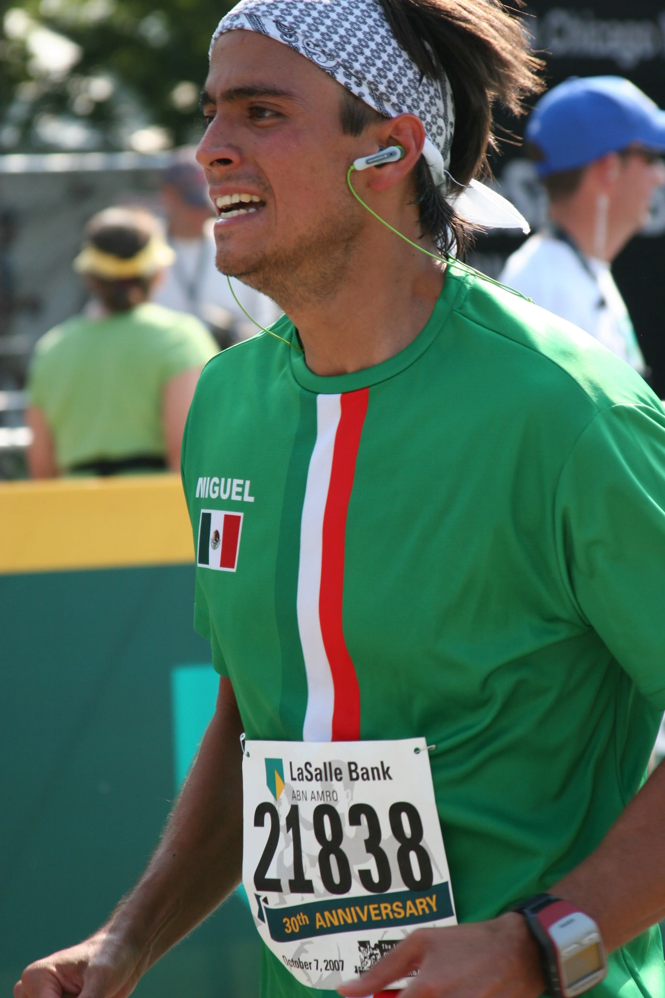 Close-up of a male marathon runner wearing a green shirt with red, white, and green stripes, a bandana, and a watch, running with a race bib number 21838 at an outdoor event on October 7, 2007.