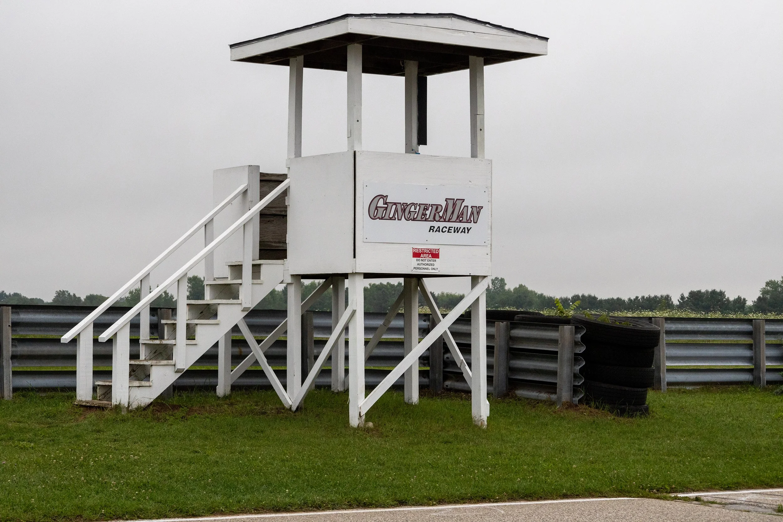 Empty white raceway tower with stairs and a sign that says 'GingerMan Raceway' and 'Restricted Area' against a cloudy sky backdrop.