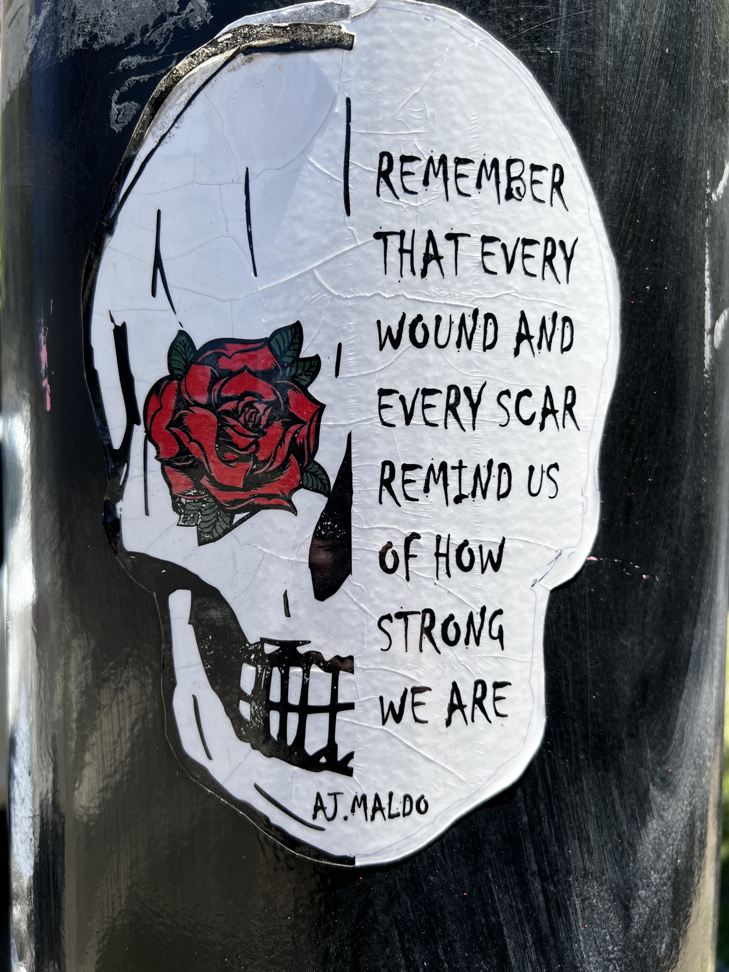 A sticker with a picture of a human skull and a red rose on the forehead, with a quote that reads, 'I remember that every wound and every scar remind us of how strong we are' by A.J. Maldo.