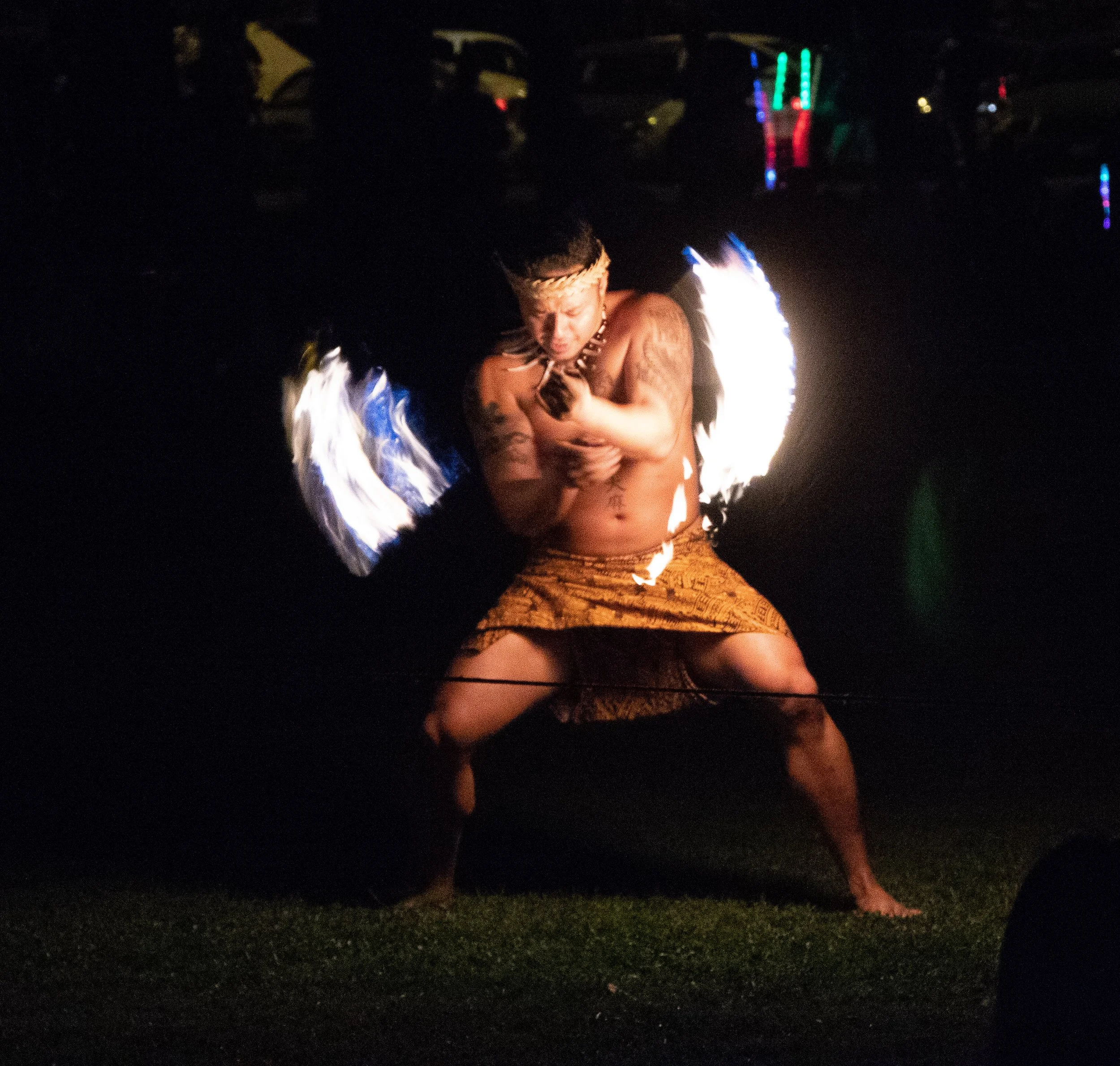 A person performing a fire spinning or fire dancing act at night, with flames creating bright light and patterns in the dark background.