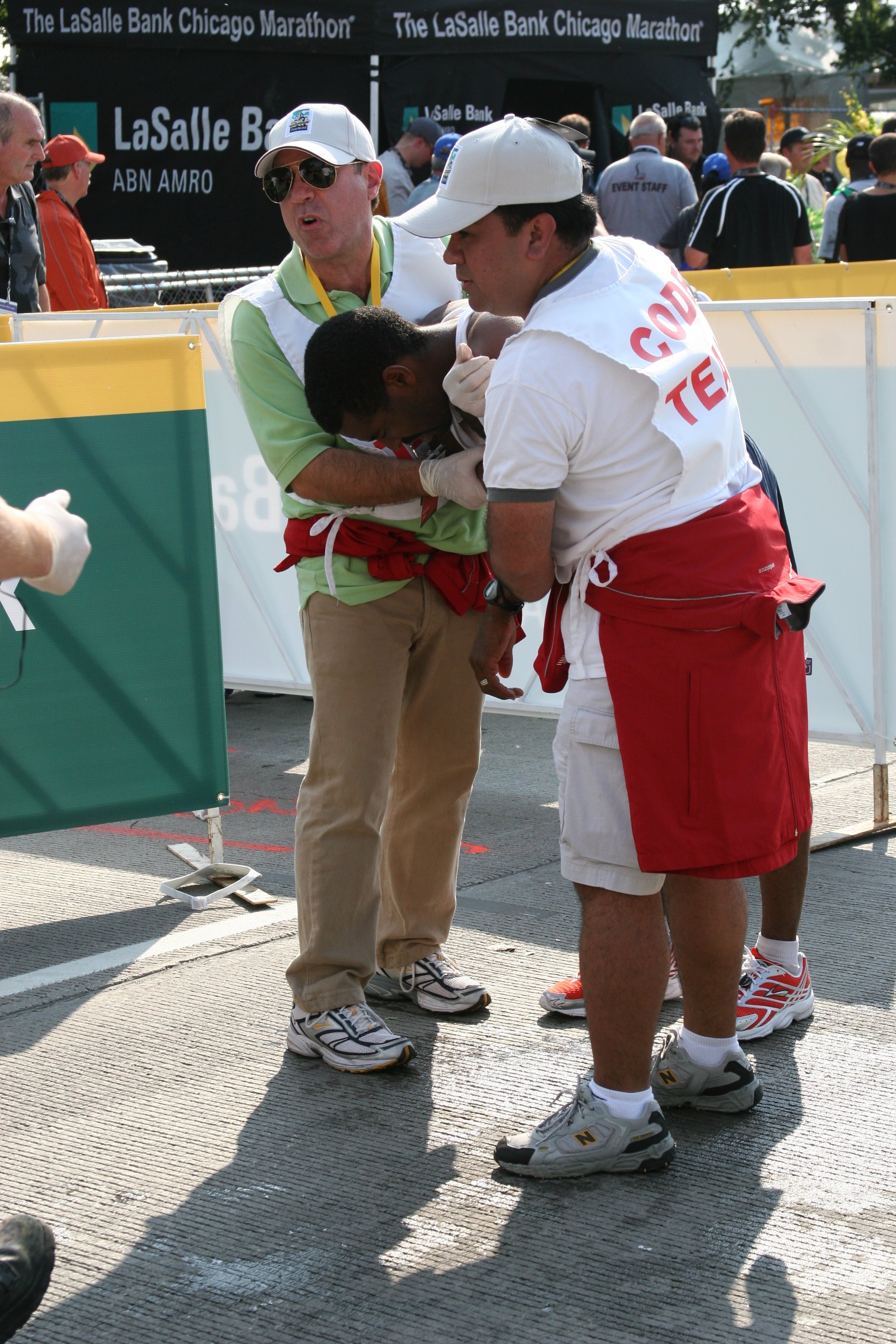 Medical personnel attending to a runner at the Chicago Marathon finish line, with many spectators and event staff in the background.