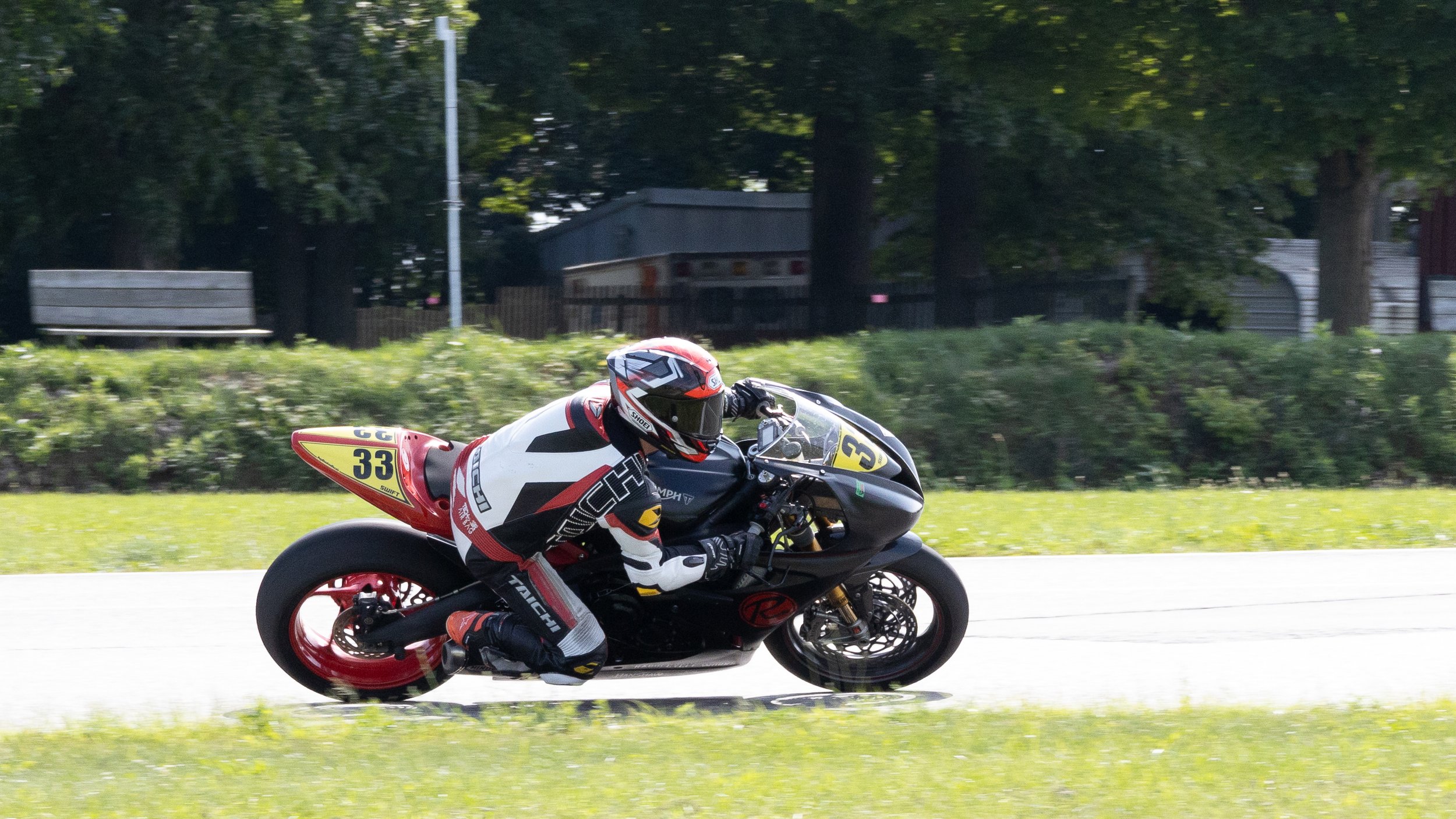A motorcyclist wearing a red and white racing suit and helmet riding a black and red sport motorcycle on a suburban street.