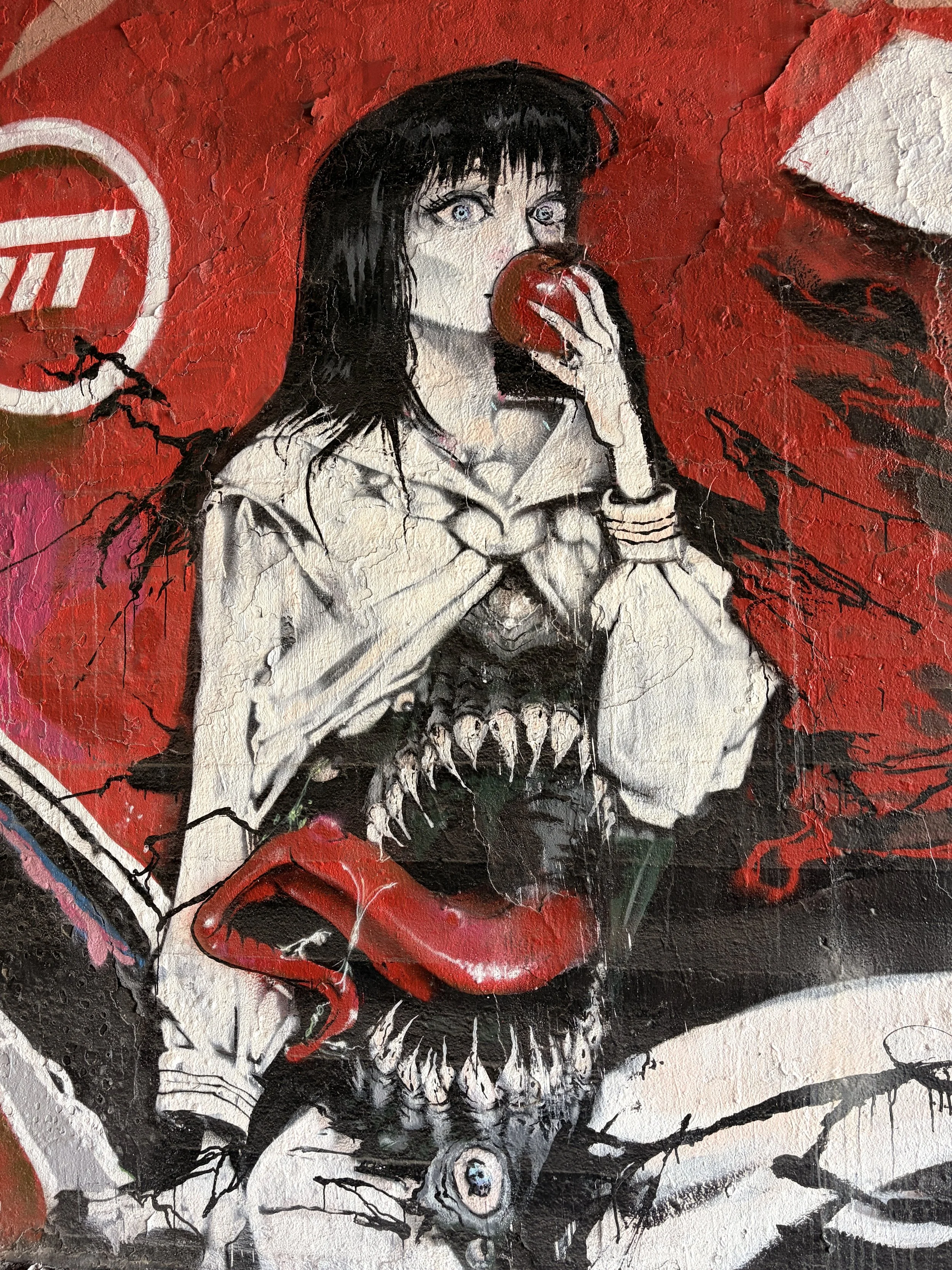 Street art painting of a woman with black hair and light skin holding a red apple up to her lips, with a red background and a large white circular symbol on the left.