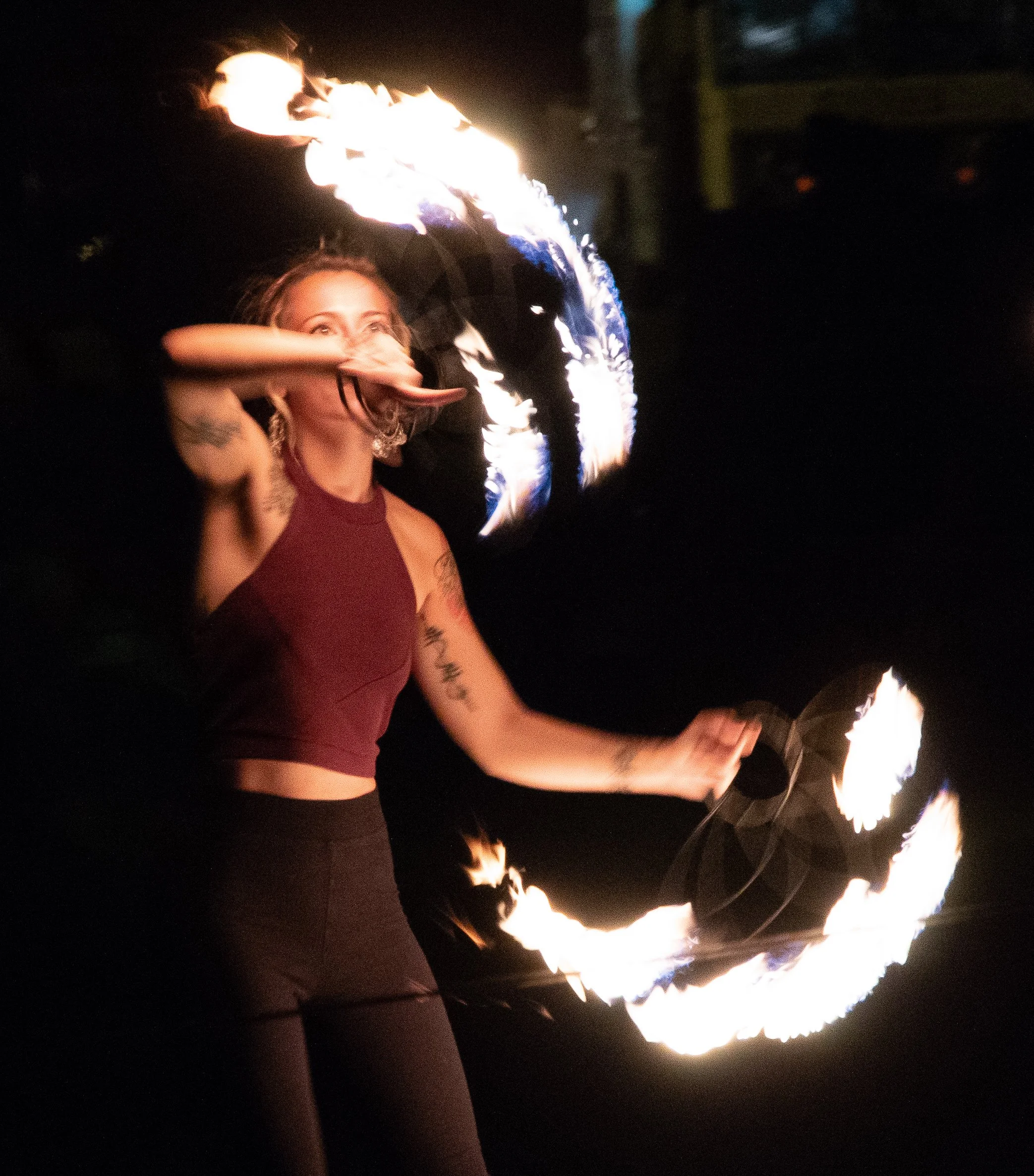 A person performing a fire show, spinning fire torches in a circle at night, with flames illuminating the surroundings.