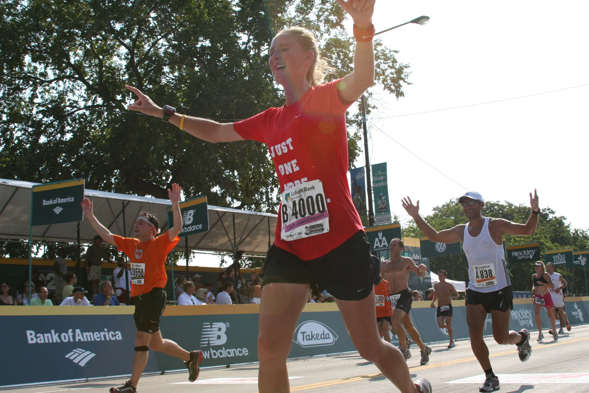 Marathon runners crossing finish line at Chicago Marathon, with spectators and race banners in the background, some runners with arms raised in celebration.