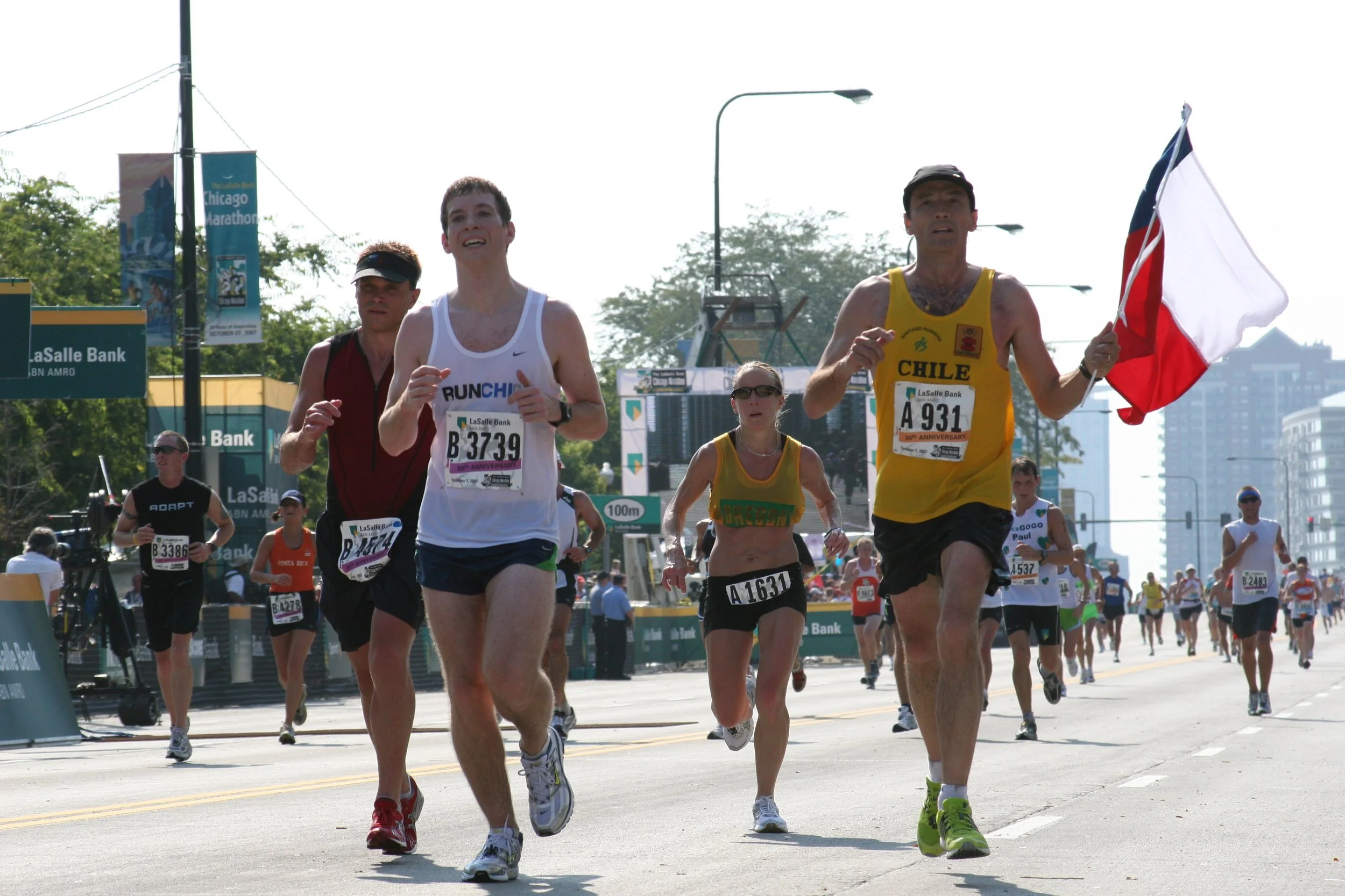Marathon runners participating in a race, with one runner holding a flag, on a city street with signs and trees in the background.
