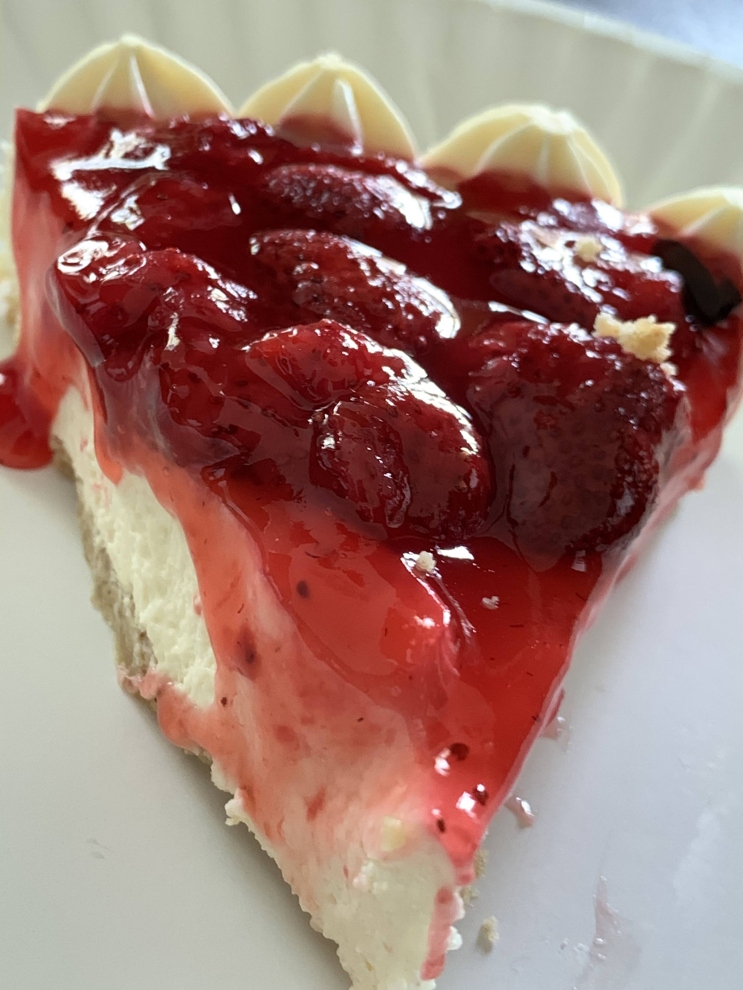 Close-up of a slice of cheesecake topped with red fruit gelatin and fresh strawberries.