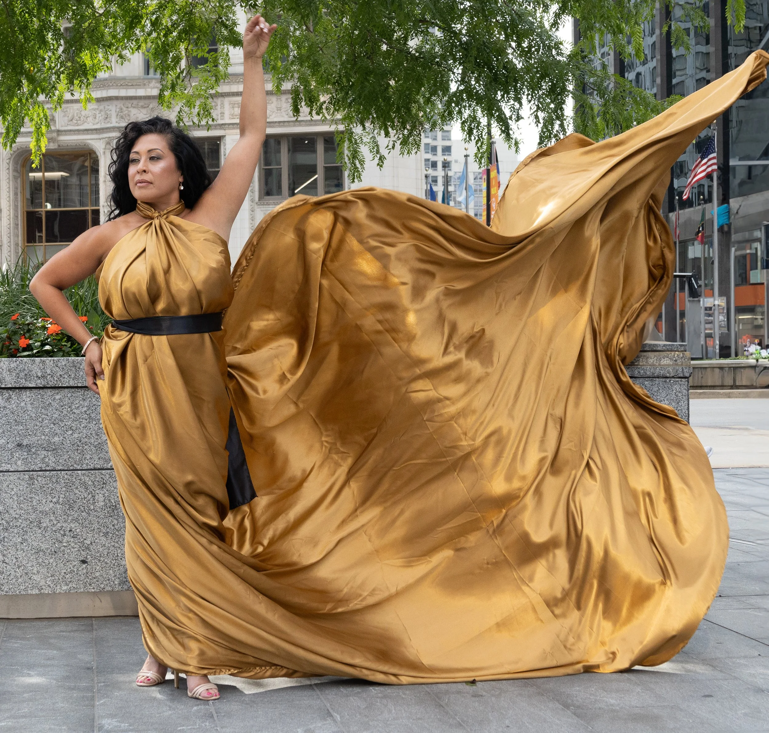Woman in a gold evening gown, standing outdoors under a tree, with the dress flowing around her.