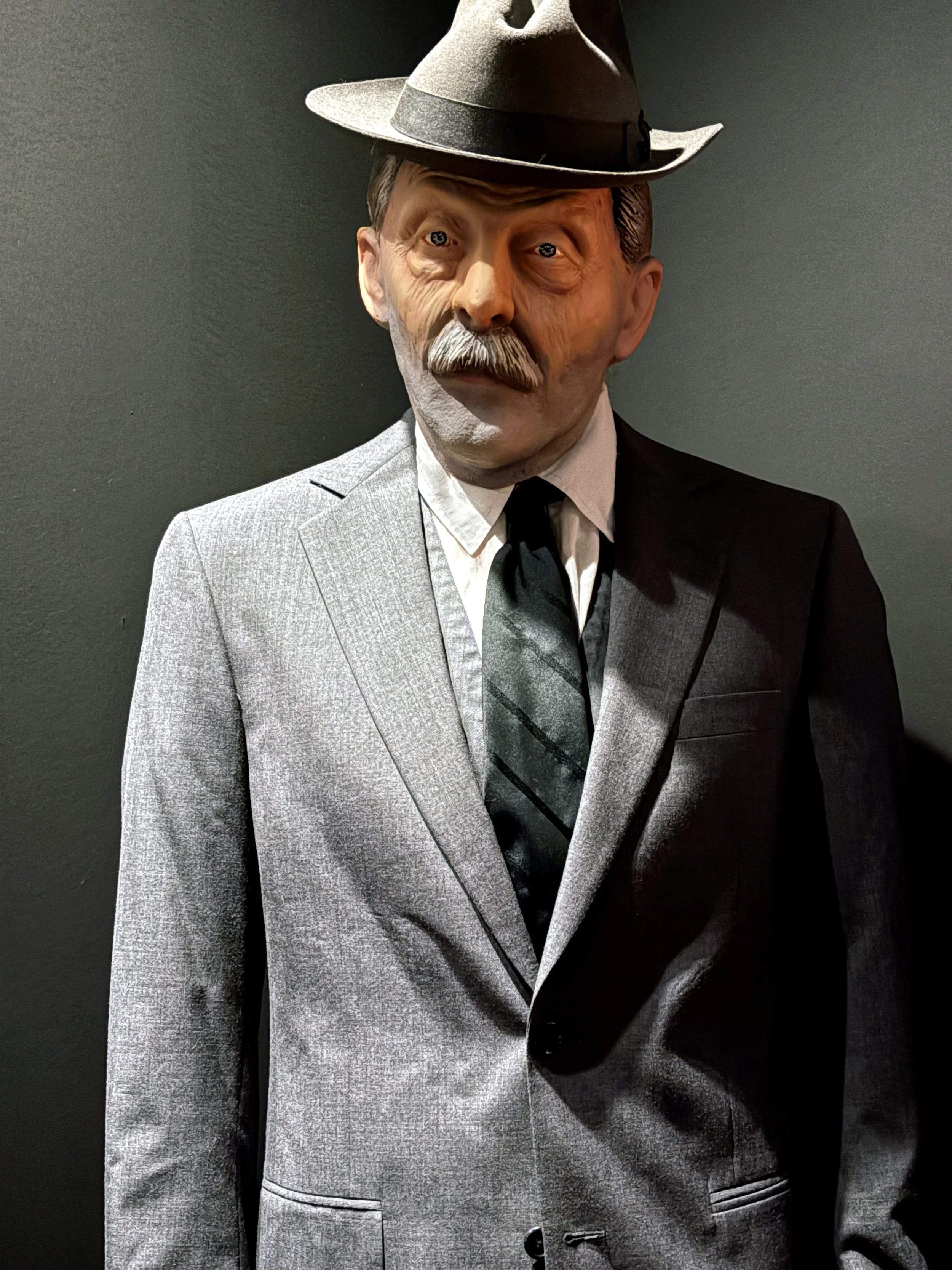 Gray suit with black tie on a person wearing a black cowboy hat against a dark background.