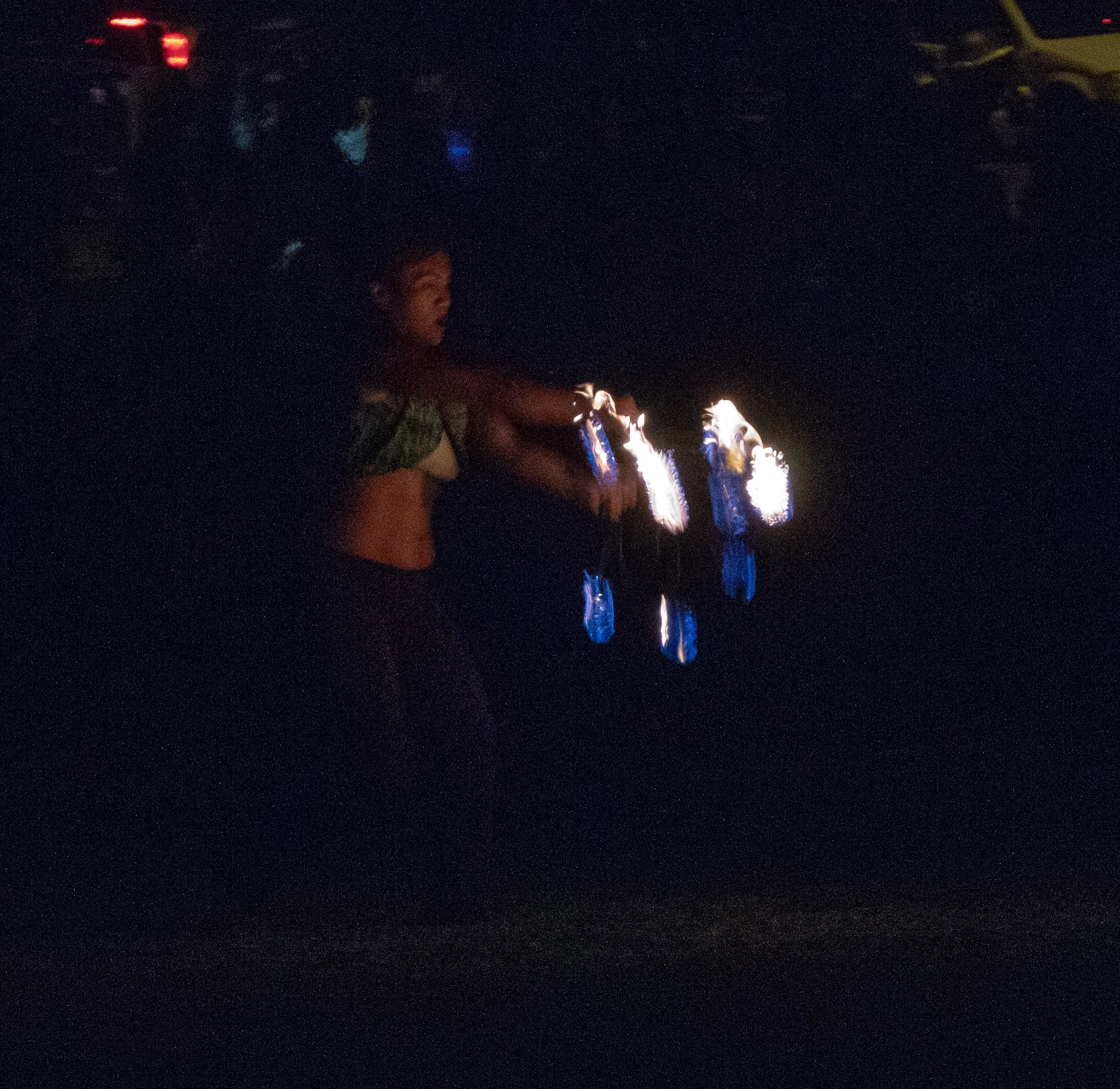 A person standing on a dark street at night, holding fireworks or sparklers that are lit and producing bright sparks.