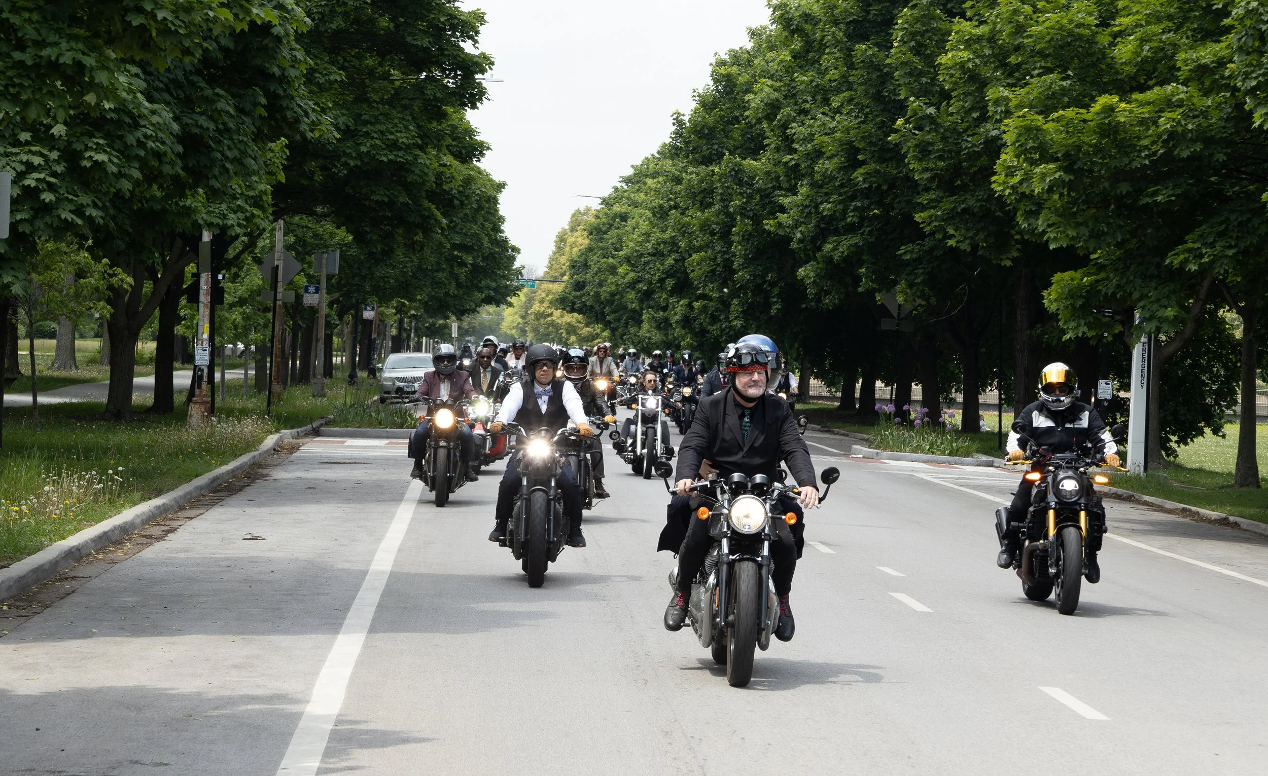 A group of motorcyclists wearing helmets riding on a tree-lined street.