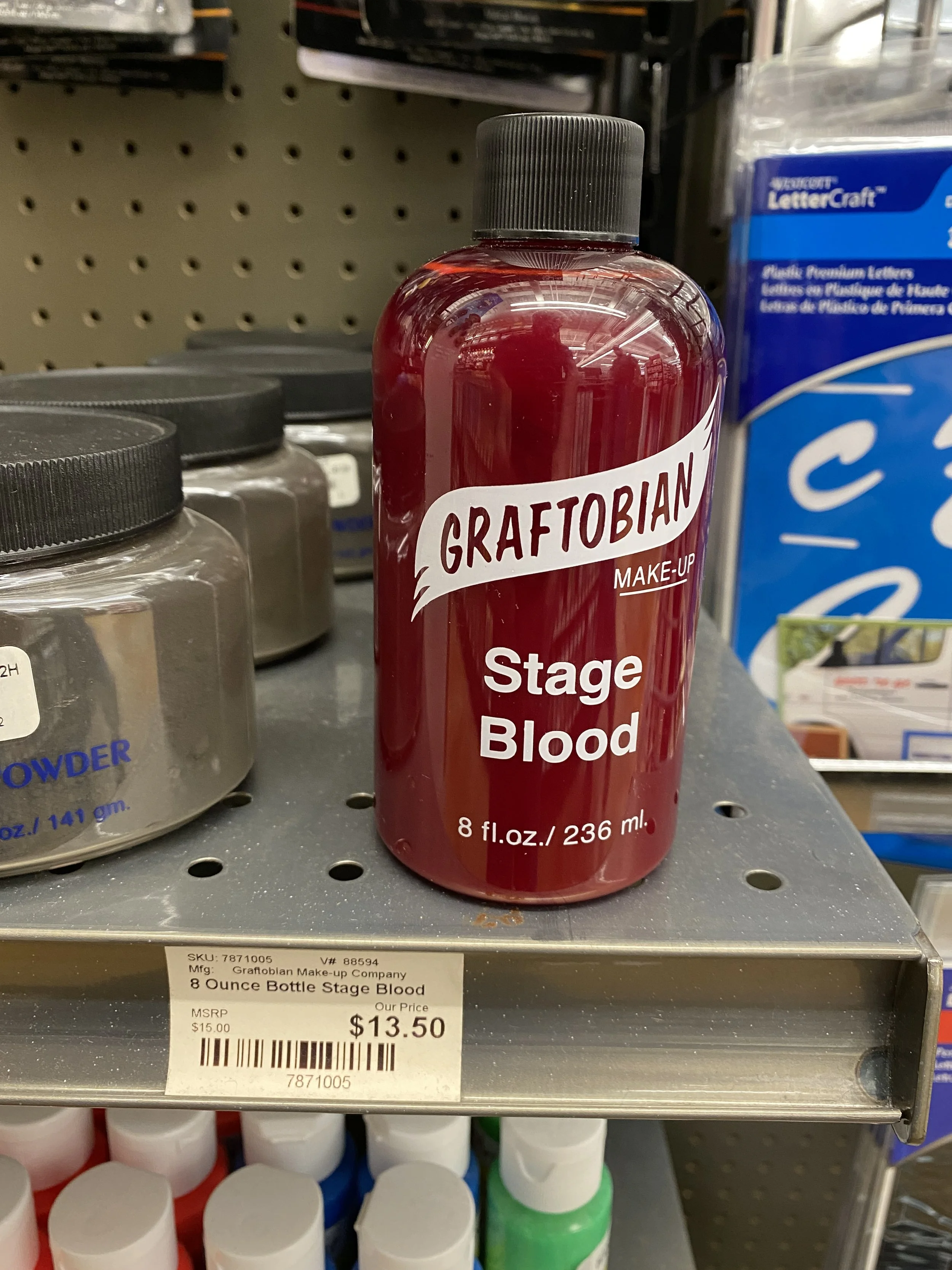 A bottle of stage blood labeled 'Graftobian Stage Blood' on store shelf alongside other bottles and supplies.