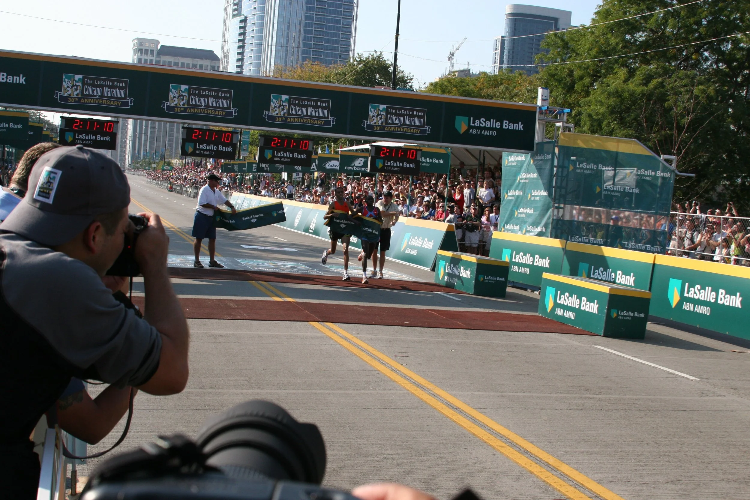 Marathon runners crossing the finish line at the Chicago Marathon, with spectators and city buildings in the background.