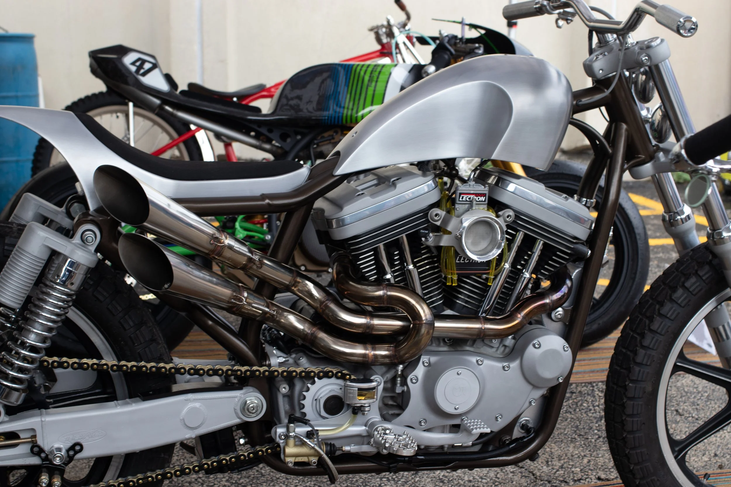 Close-up of a custom motorcycle with metallic silver bodywork, chrome exhaust pipes, and visible engine components, parked outdoors.