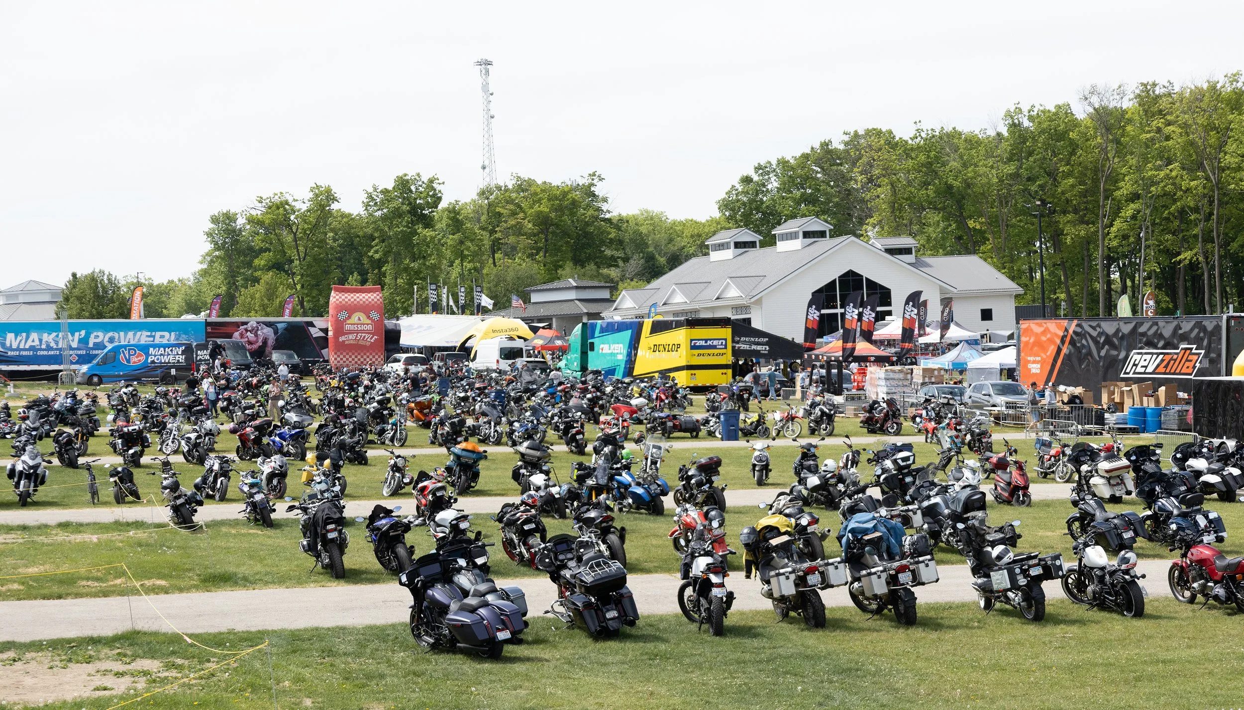 Outdoor motorcycle parking area with numerous motorcycles, event tents, and banners.