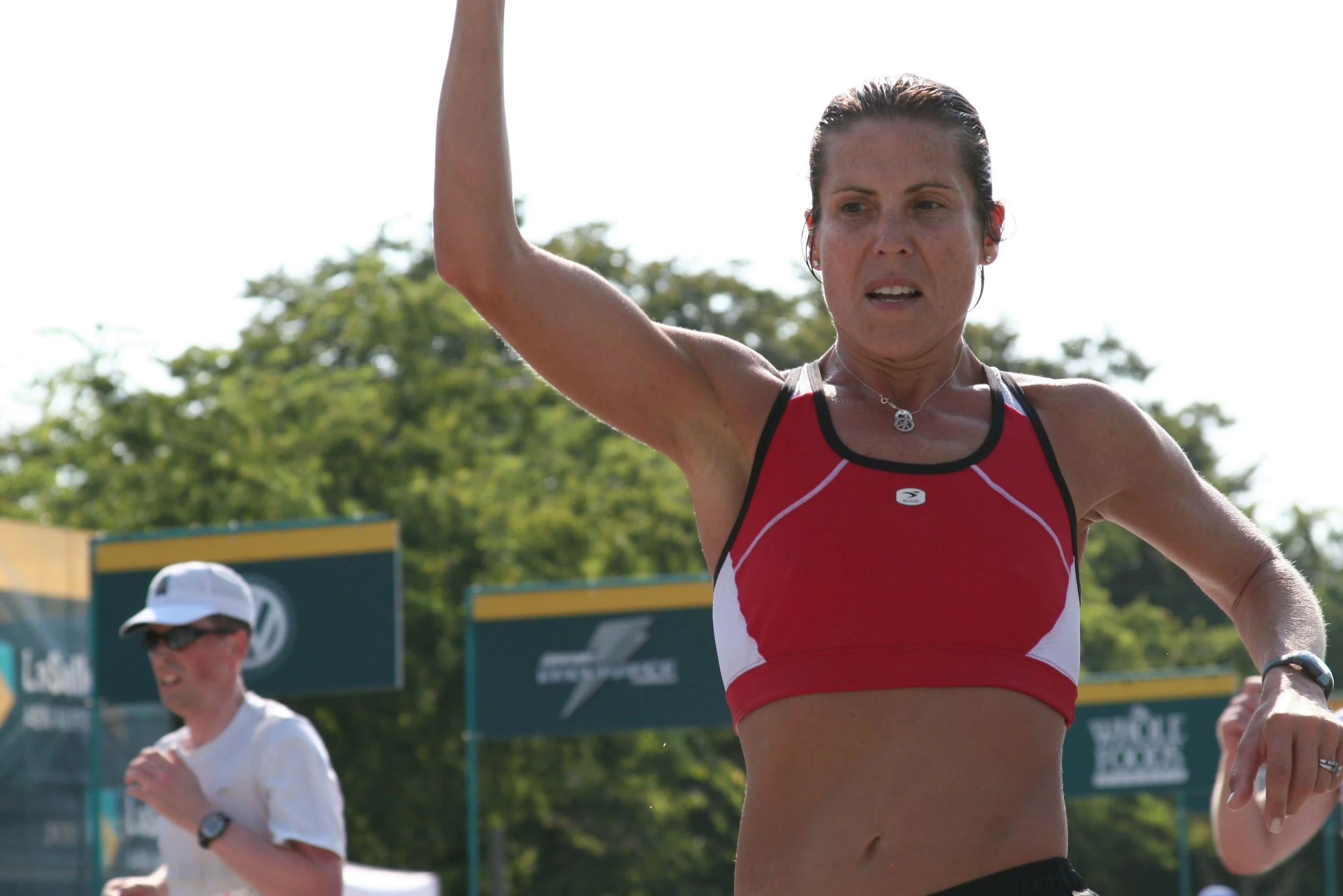 A woman in athletic gear participating in a running event outdoors, with trees and a cloudy sky in the background.