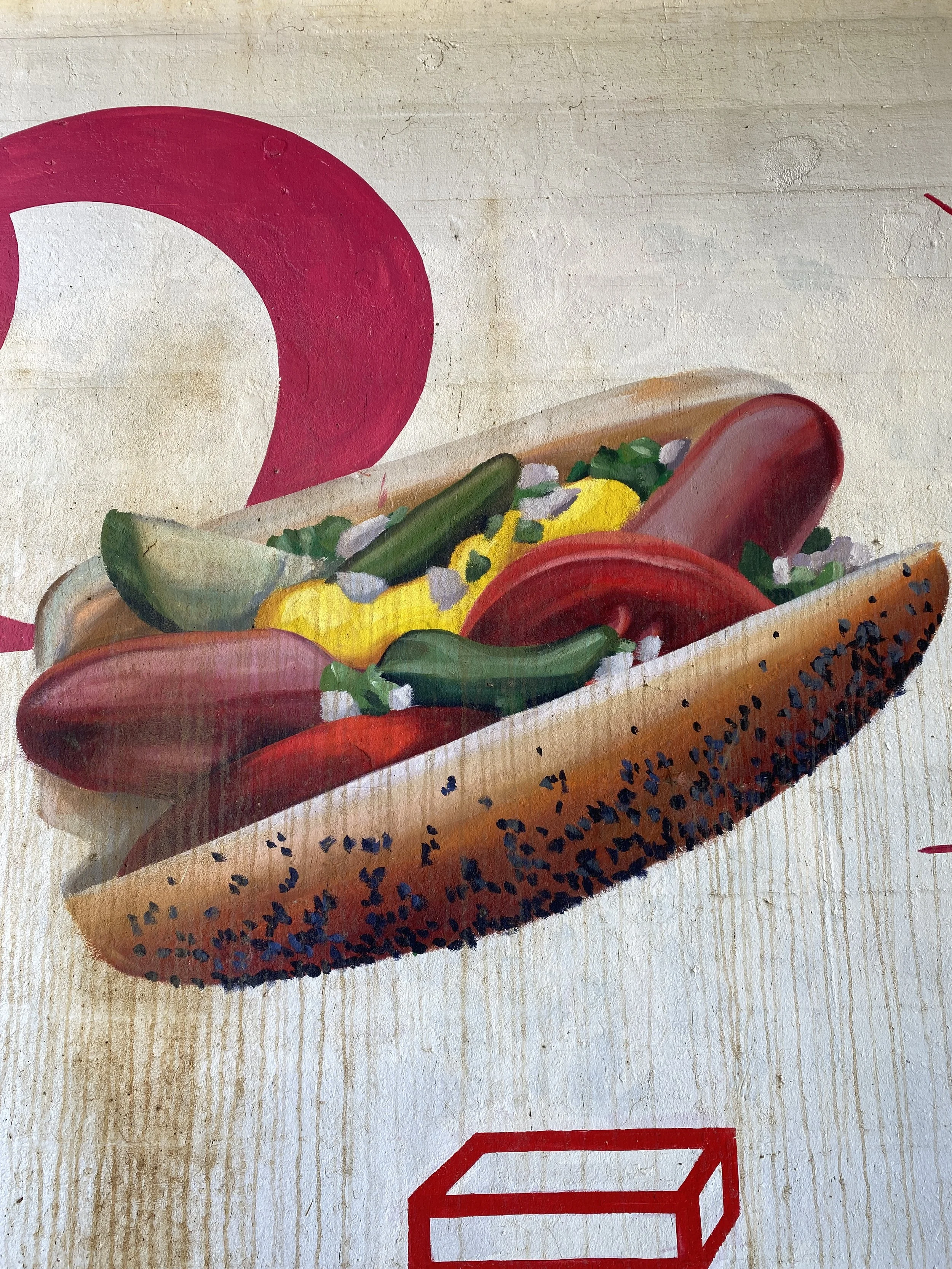 A detailed painting of a hot dog with mustard, pickles, onions, and toppings in a bun, with a large pink number 2 in the background and a red geometric shape in the foreground.