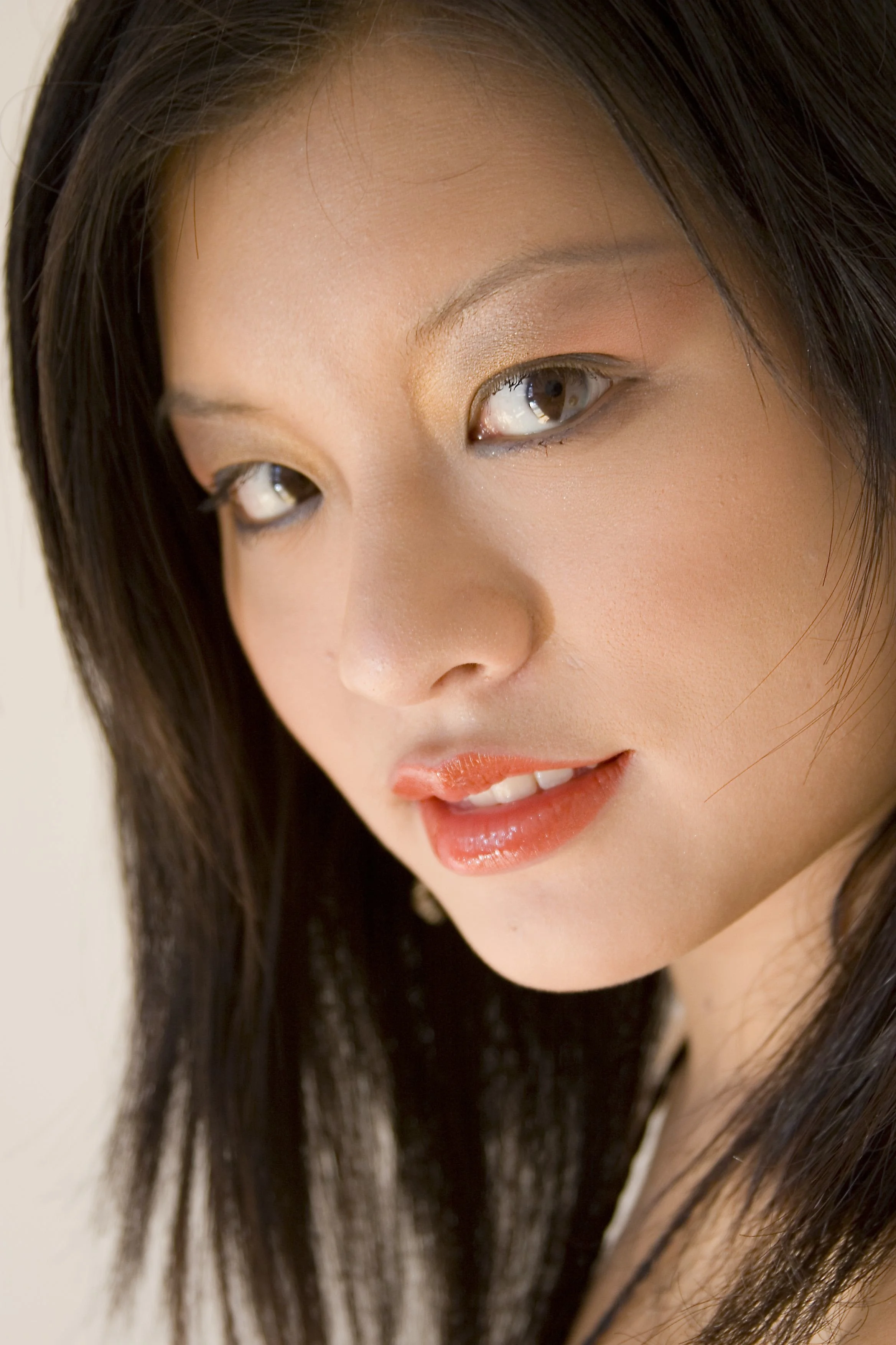 Close-up of a woman's face with dark hair, wearing makeup, and a neutral background.