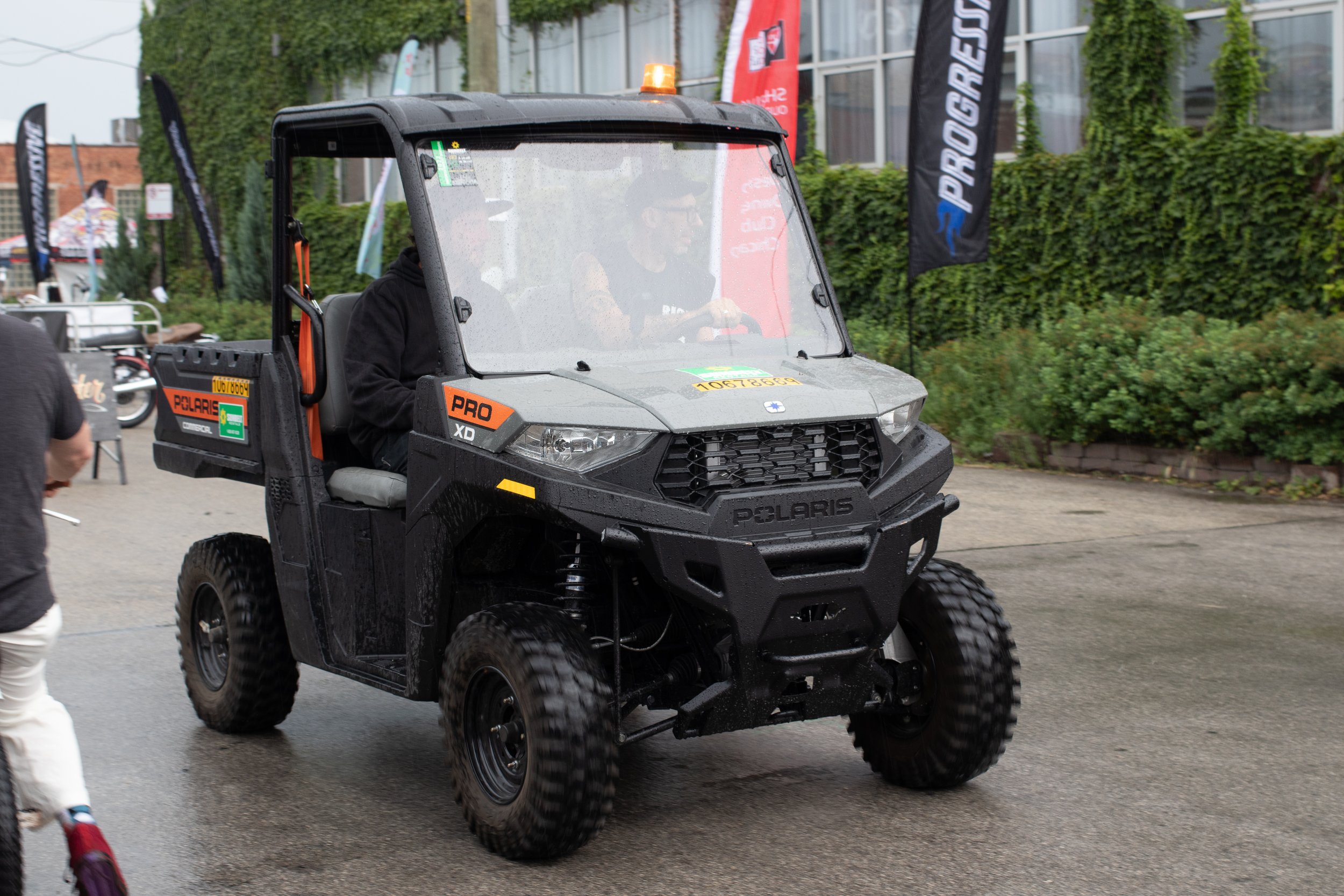 A black Polaris off-road utility vehicle with four large tires, shiny wet surface, and orange accents, parked outdoors in a paved area on a rainy day.