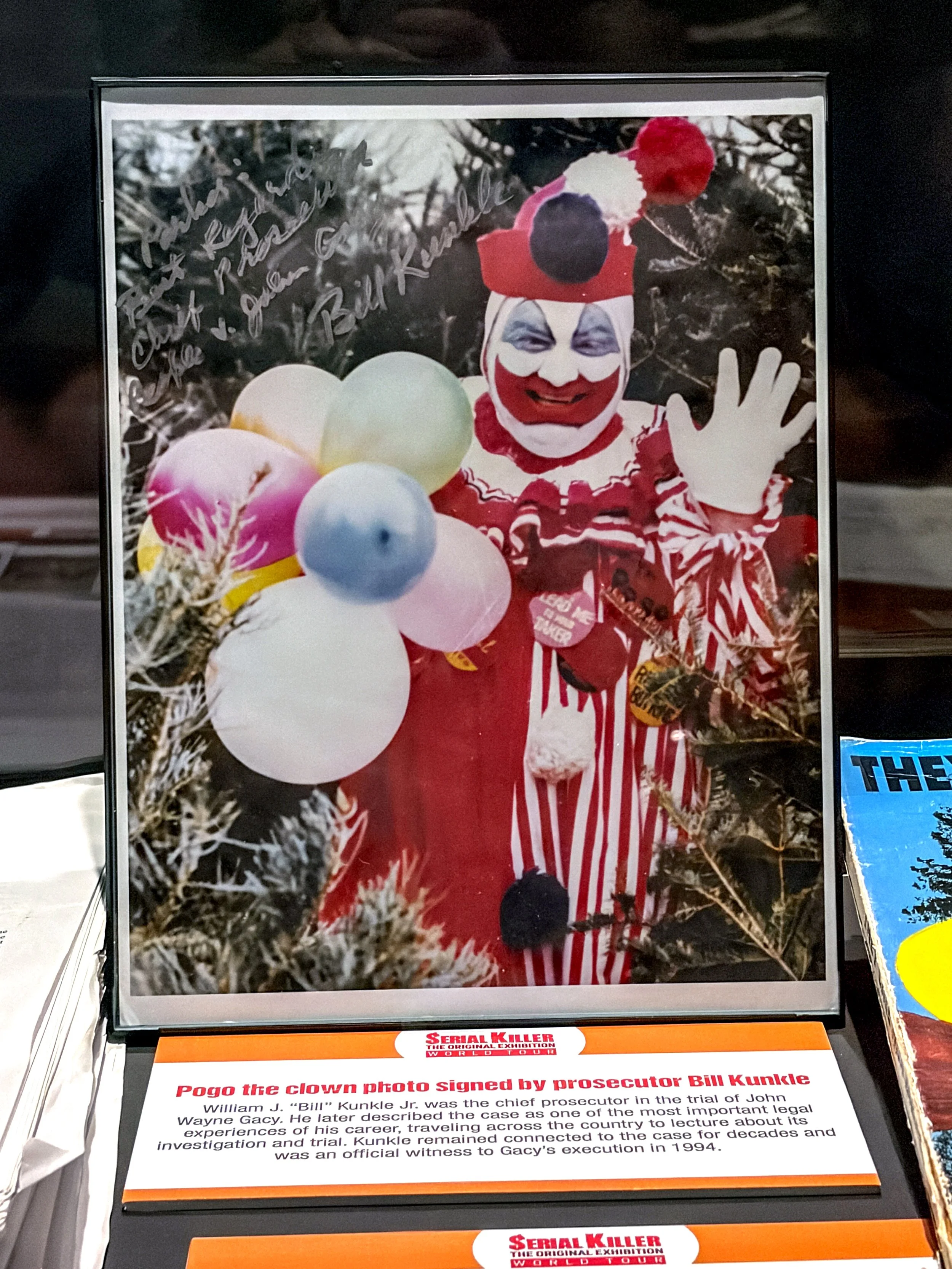 Photograph of Pogo the clown, dressed in a red and white striped costume, waving, standing among balloons at a clown exhibition.