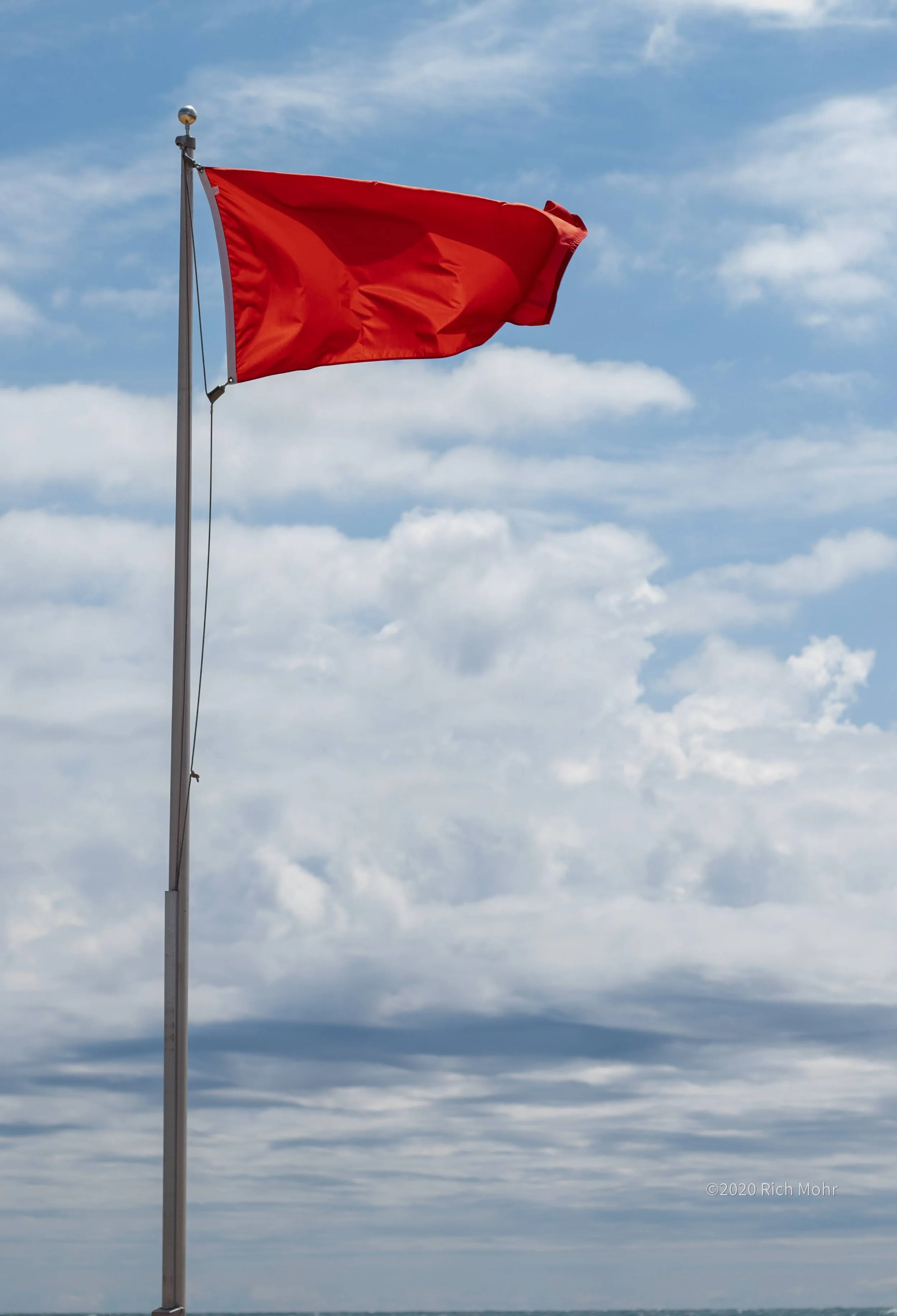 Red flag flying on a pole against a partly cloudy sky.