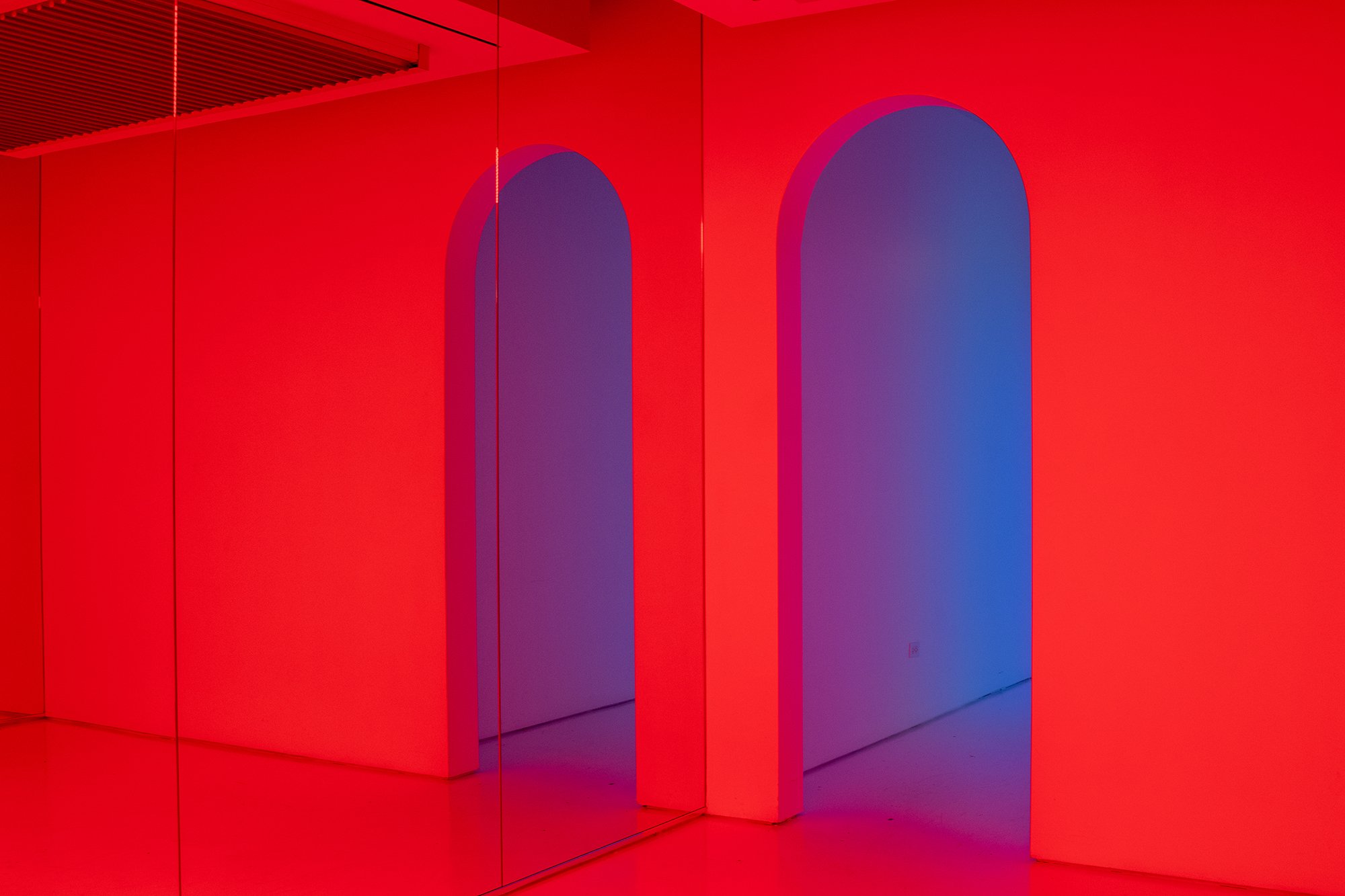 Red wall with two large arch-shaped cutouts or windows with purple inner surfaces, part of a modern interior design.