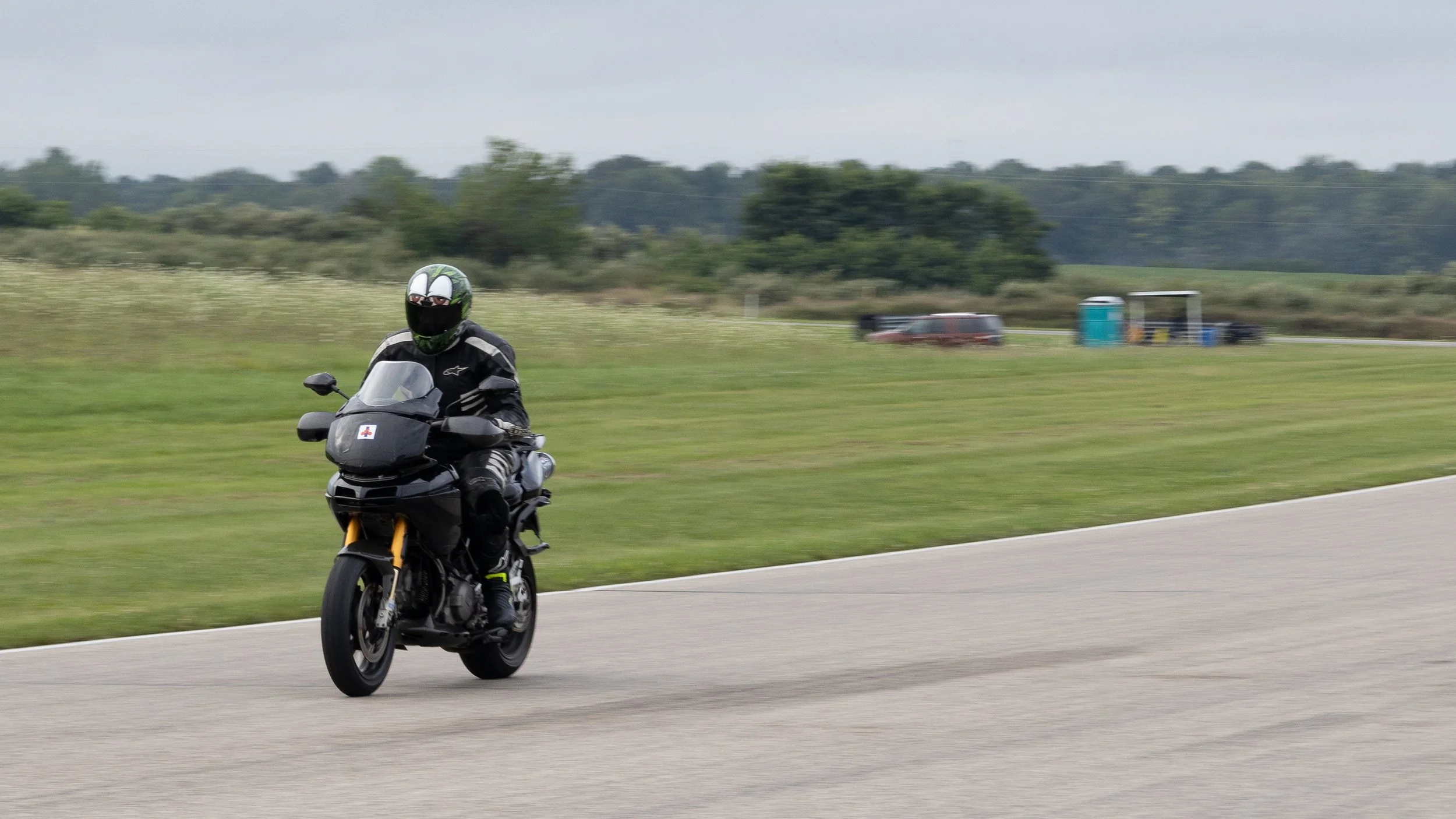 Motorcyclist wearing a helmet and riding a black motorcycle on a highway with grassy fields and trees in the background.