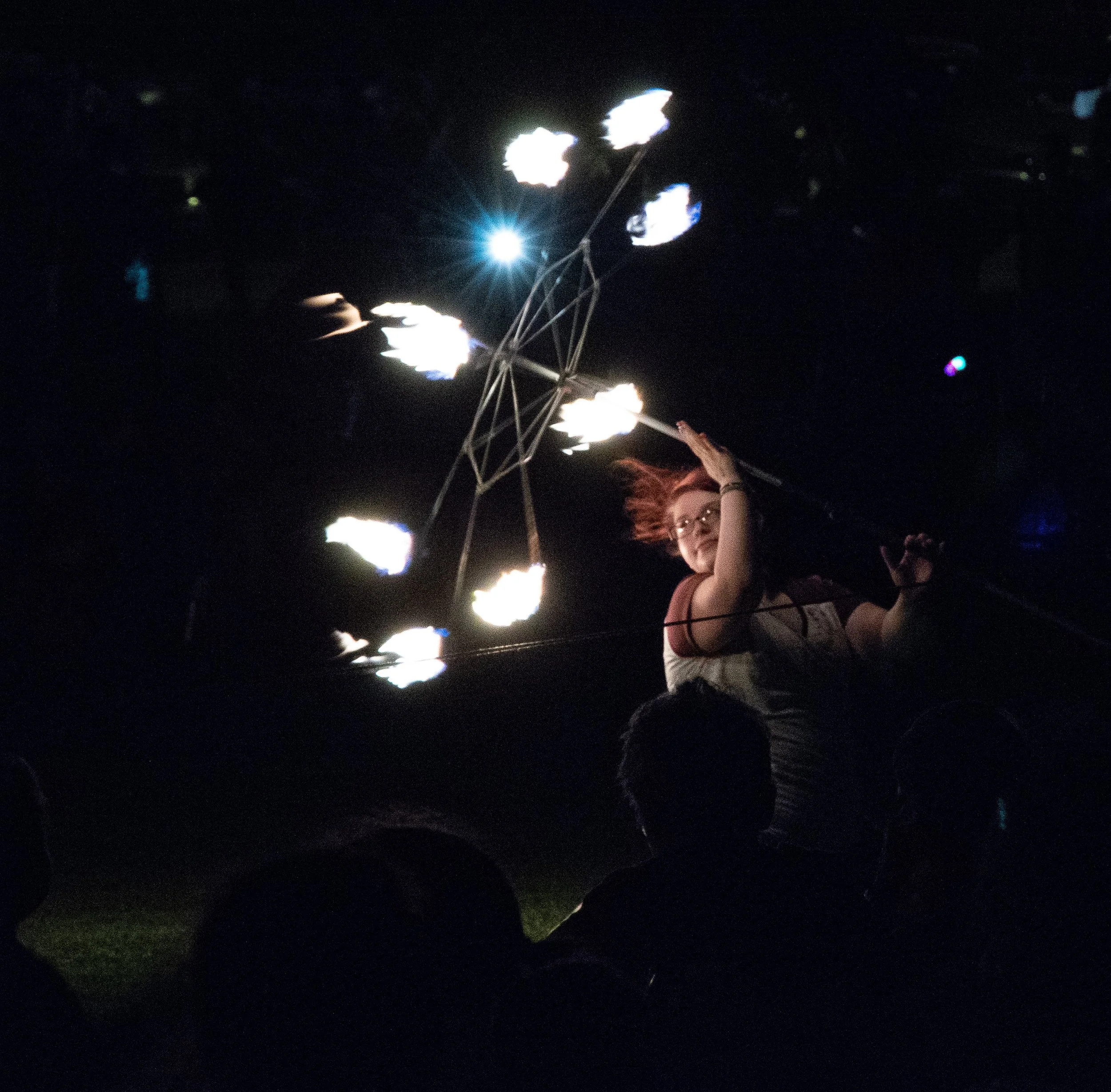 People at a nighttime event holding sparkler firework sticks, with one person in the foreground wearing glasses and a striped shirt.